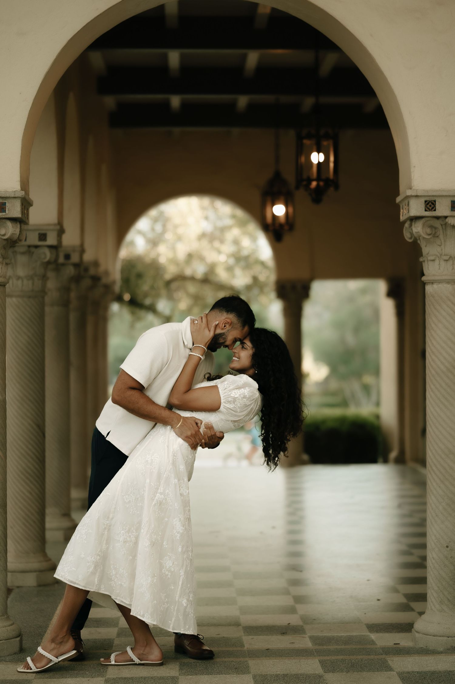 Romantic dance pose under an elegant archway with hanging lanterns.
