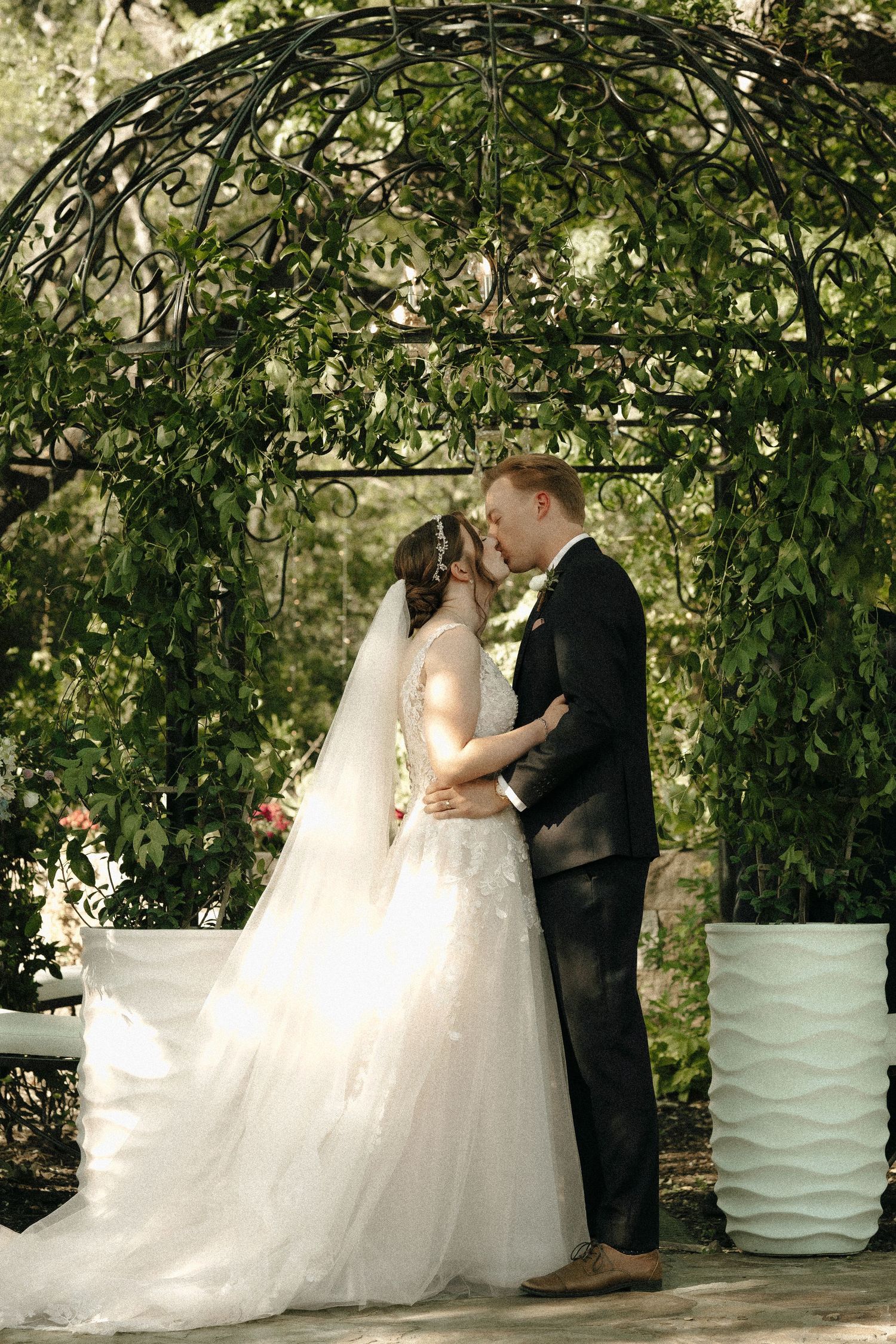 A wedding ceremony takes place under a natural archway of lush green trees and leaves.
