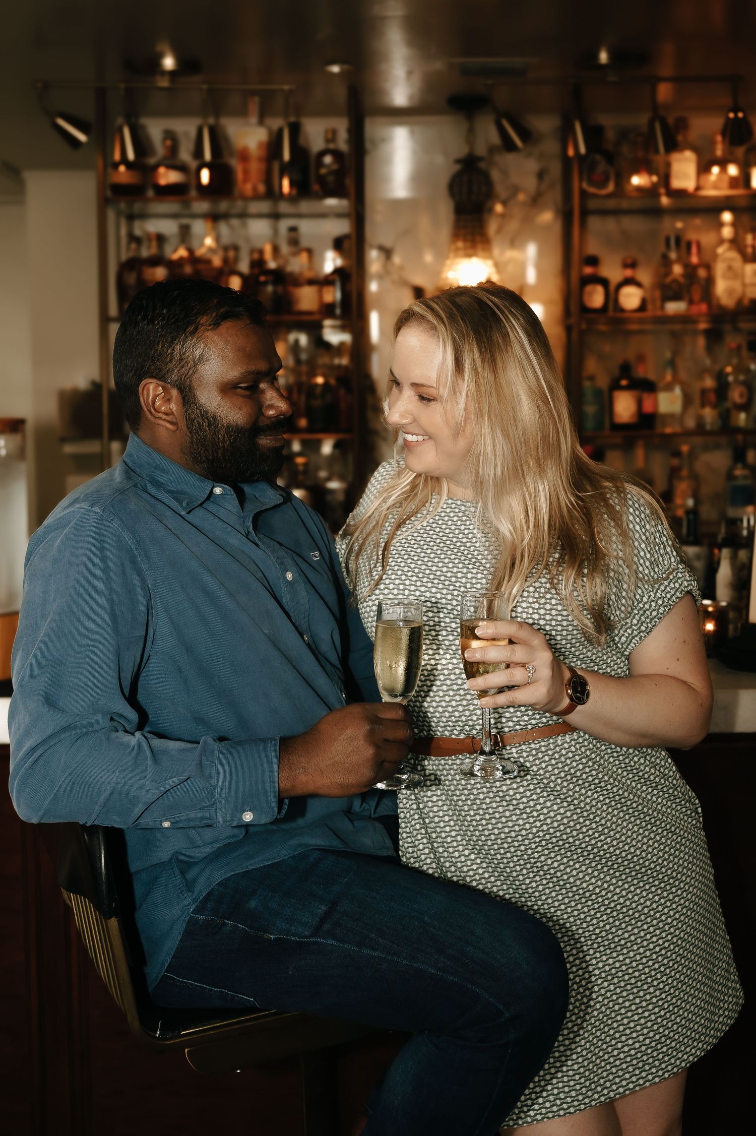 A couple shares an intimate moment together at a dimly lit bar with bottles in the background.