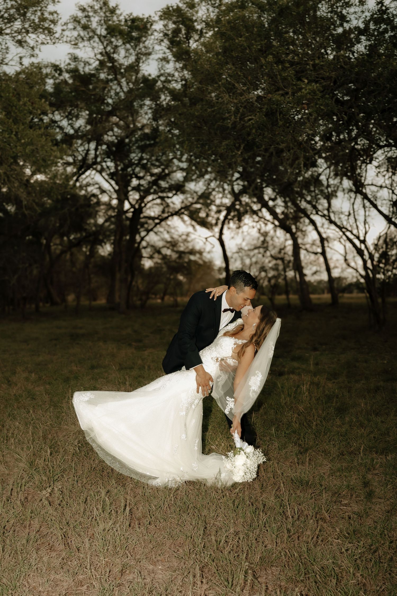 A romantic wedding photoshoot in a field at golden hour with dramatic lighting.