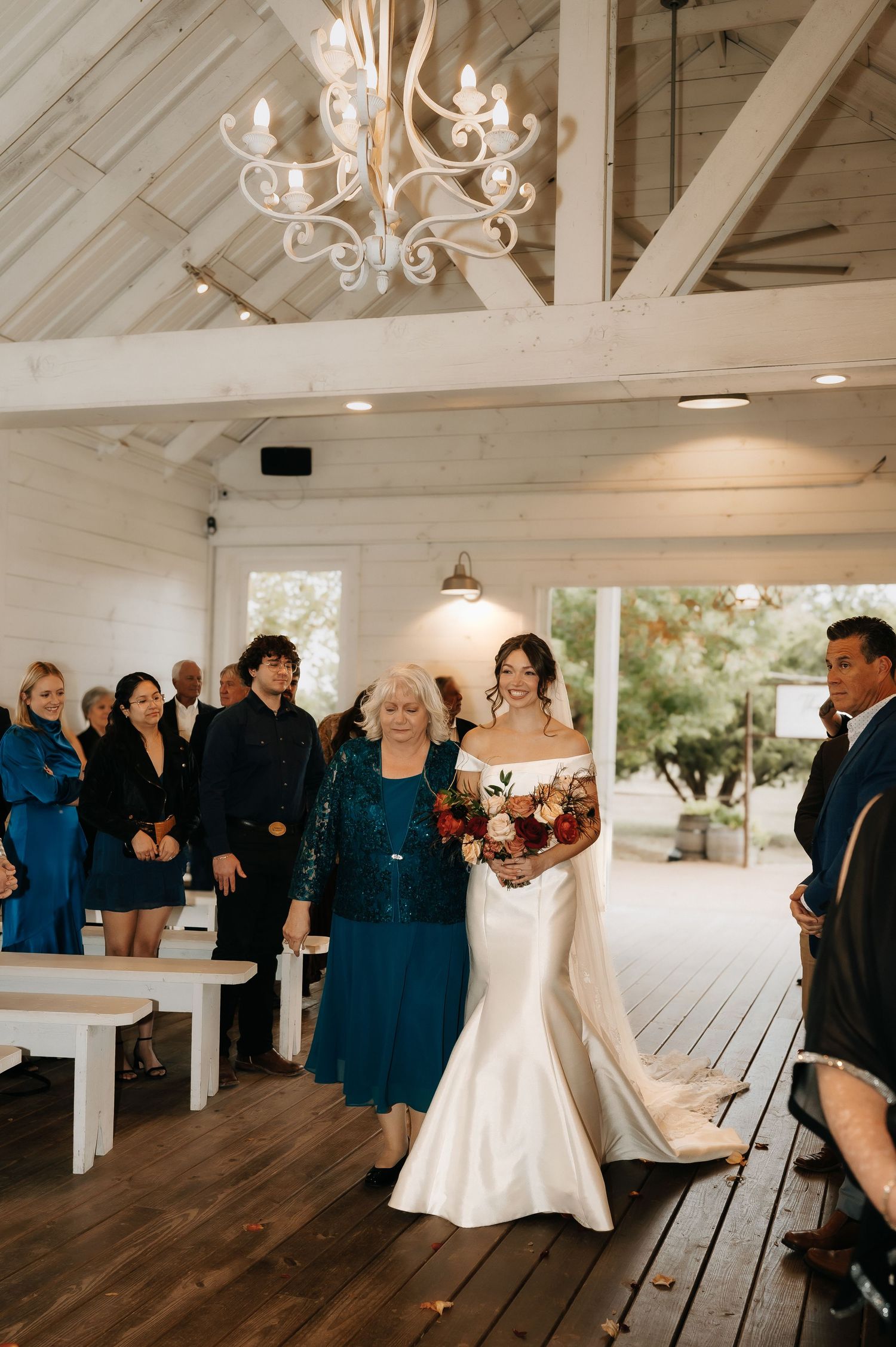 Wedding ceremony in rustic white barn venue with elegant chandelier and wooden details.