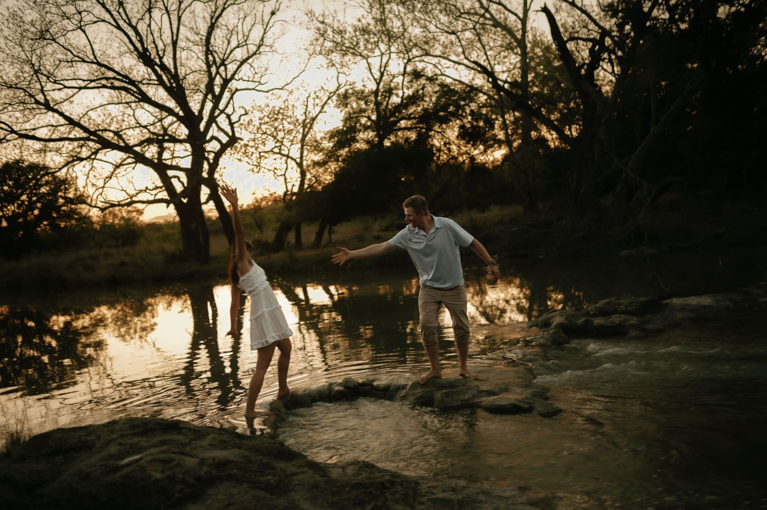 Playful couple enjoying nature by a reflective pond at sunset.