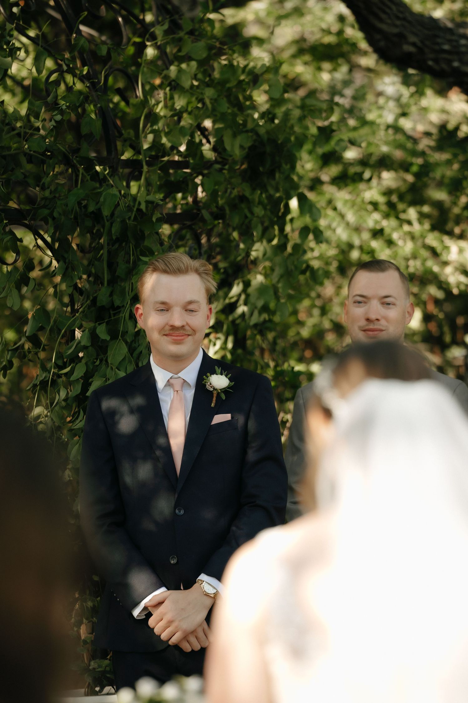 Groomsmen in dark suits with peach ties watch the wedding ceremony unfold.