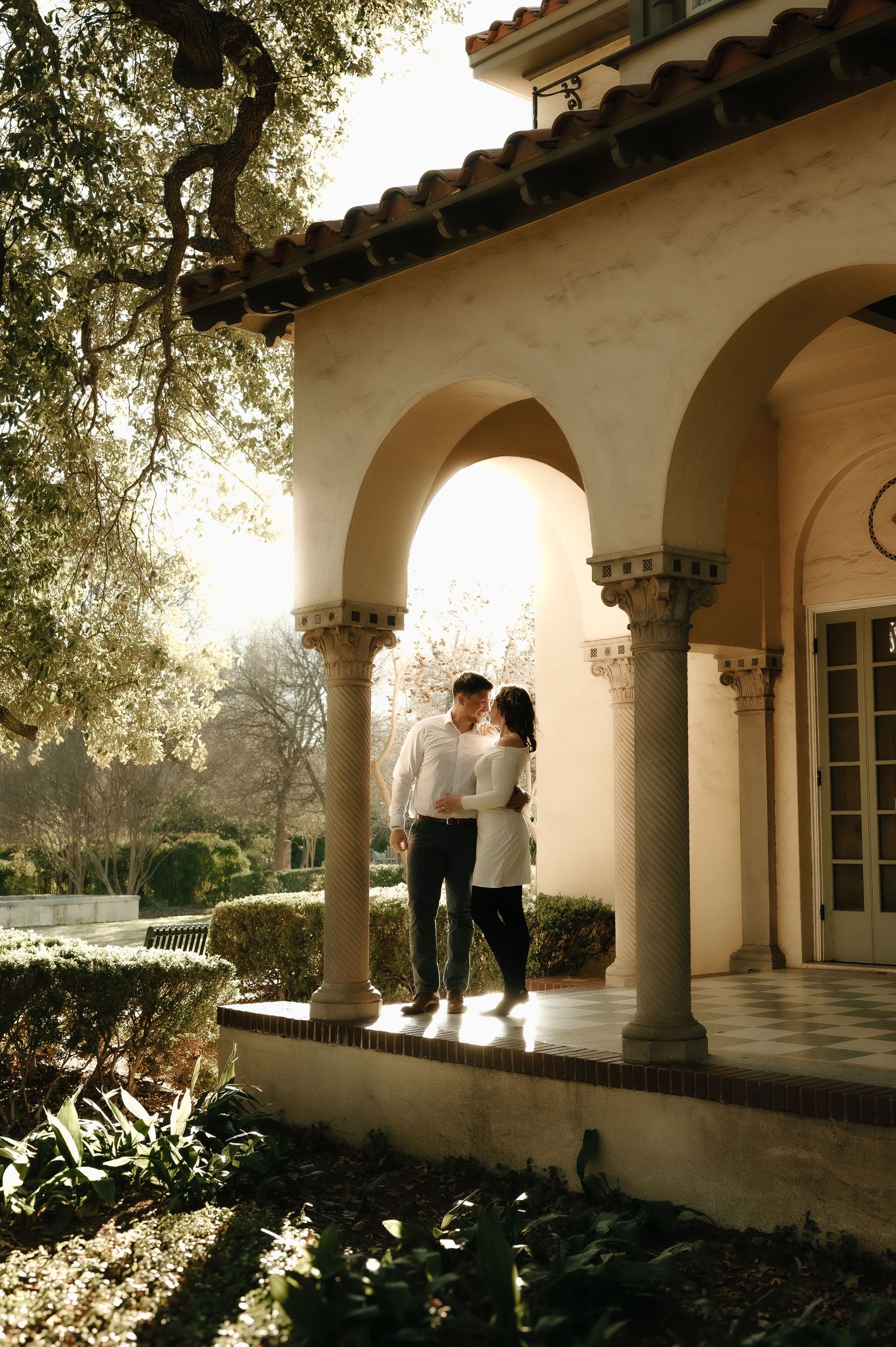 Couple walking under Spanish-style archway during golden hour.