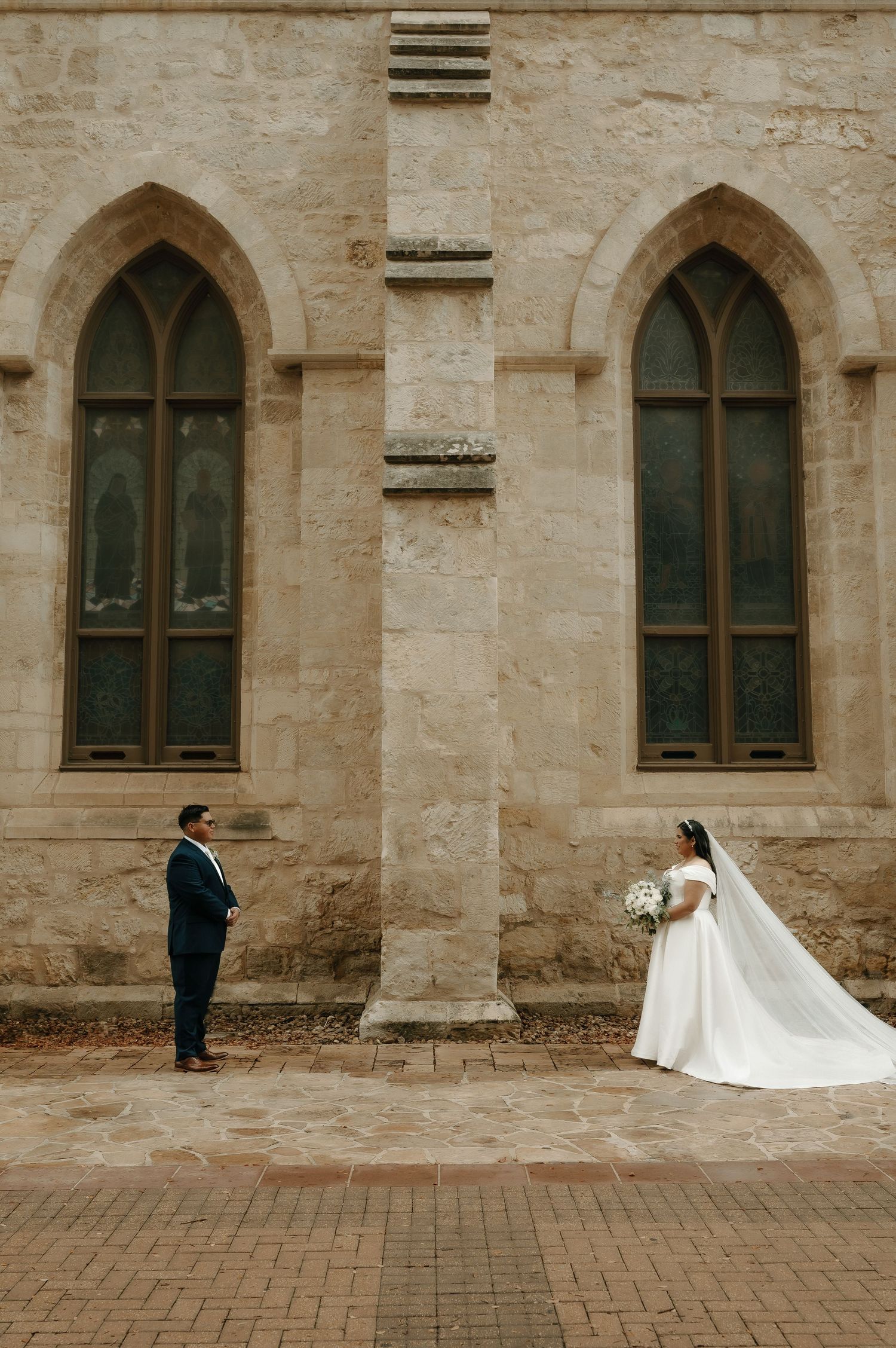 A romantic wedding photoshoot against a historic stone church with Gothic arched windows.