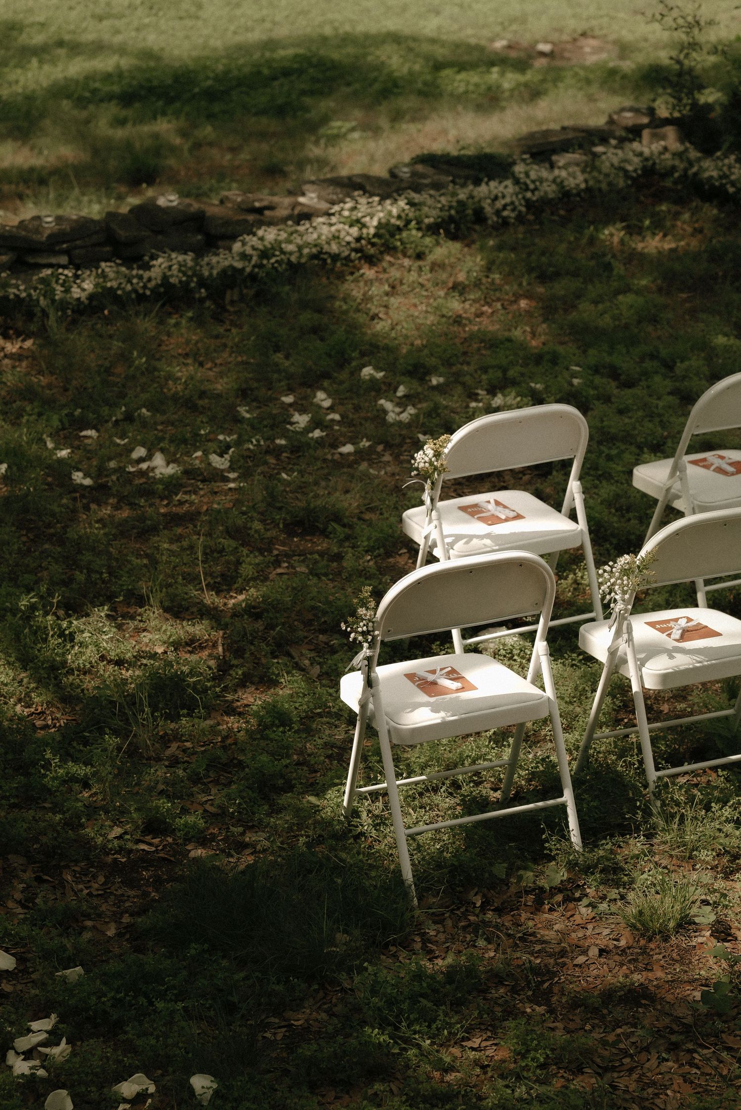 White folding chairs set up for an outdoor wedding ceremony with delicate floral decorations.