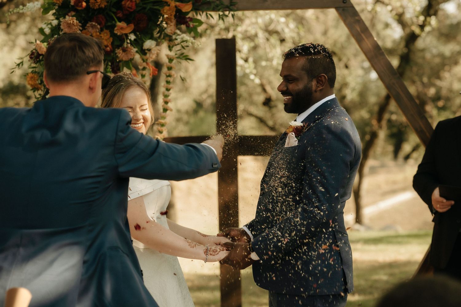 Wedding celebration moment captured under trees with glitter or confetti in the air.