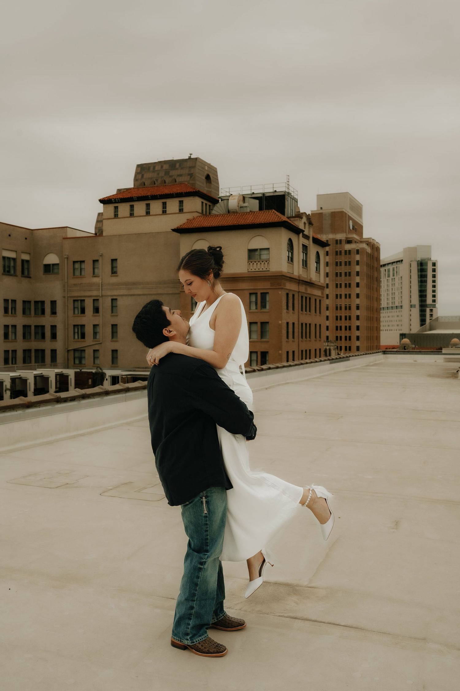 A couple dances and embraces on an urban rooftop with city buildings in the background.