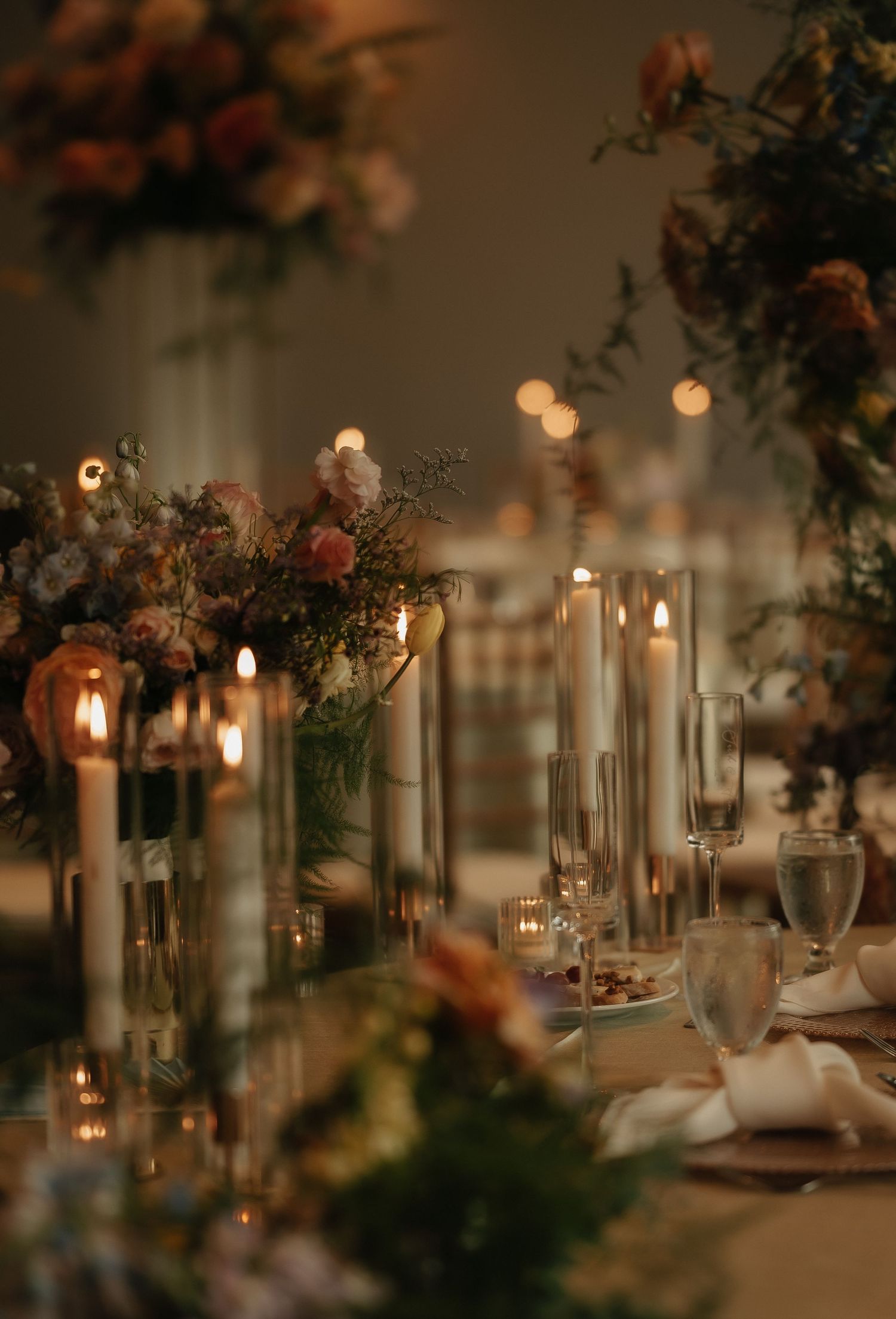 Romantic candlelit wedding reception table with floral centerpieces and glassware.