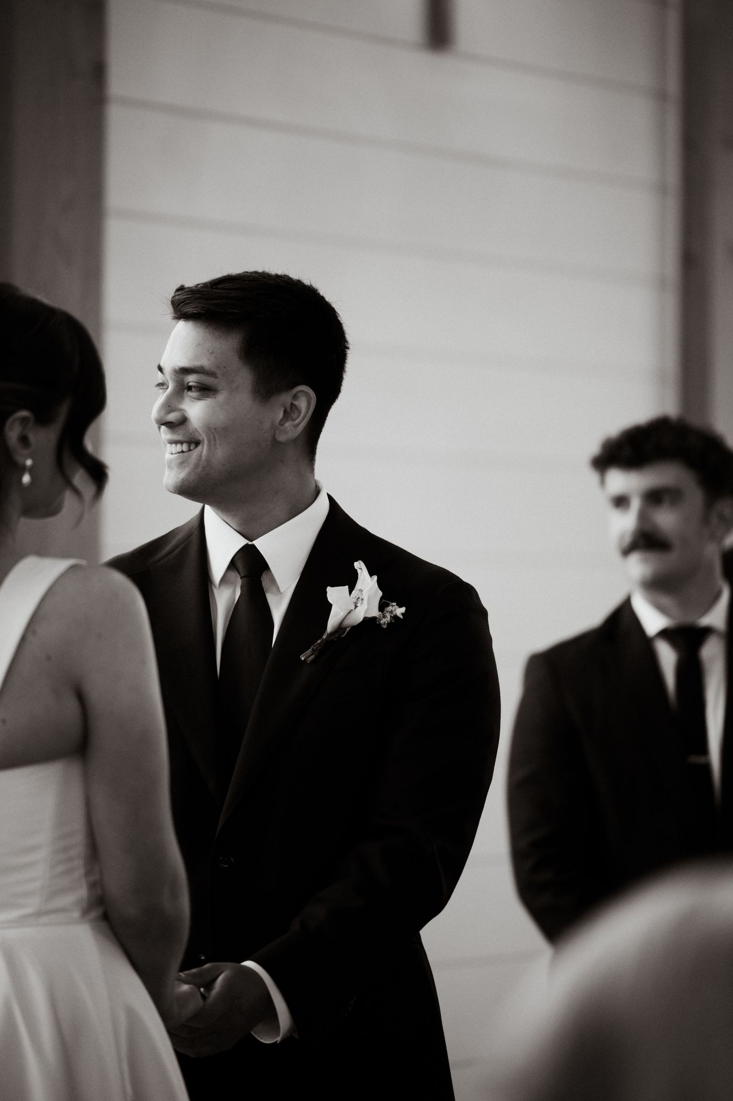Smiling groom in black suit with boutonniere stands at the altar during his wedding ceremony.