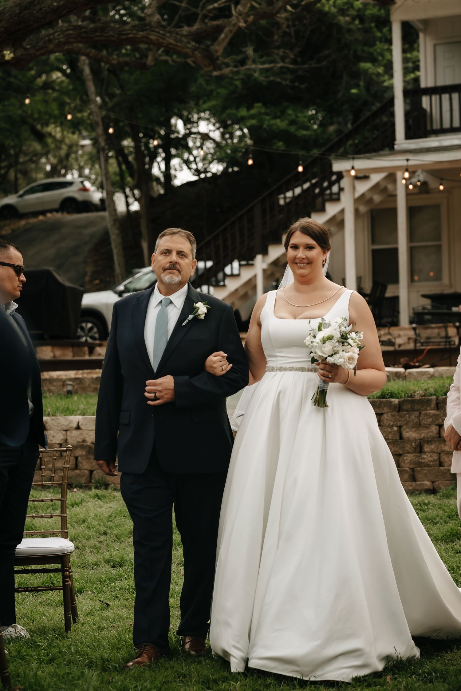 Wedding processional on grassy lawn with elegant white gown and formal attire.