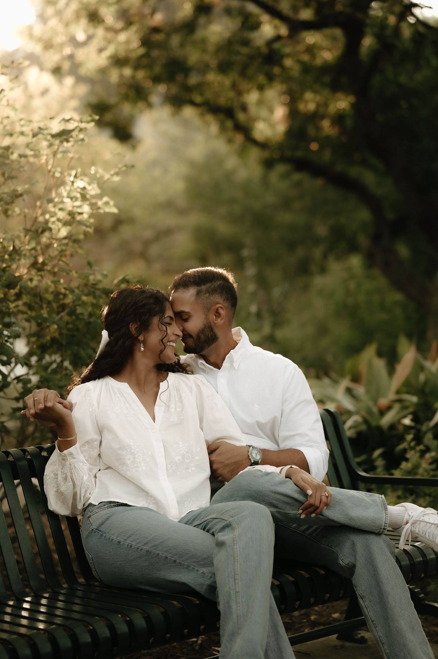 Couple sharing an intimate moment while sitting on a park bench surrounded by greenery.