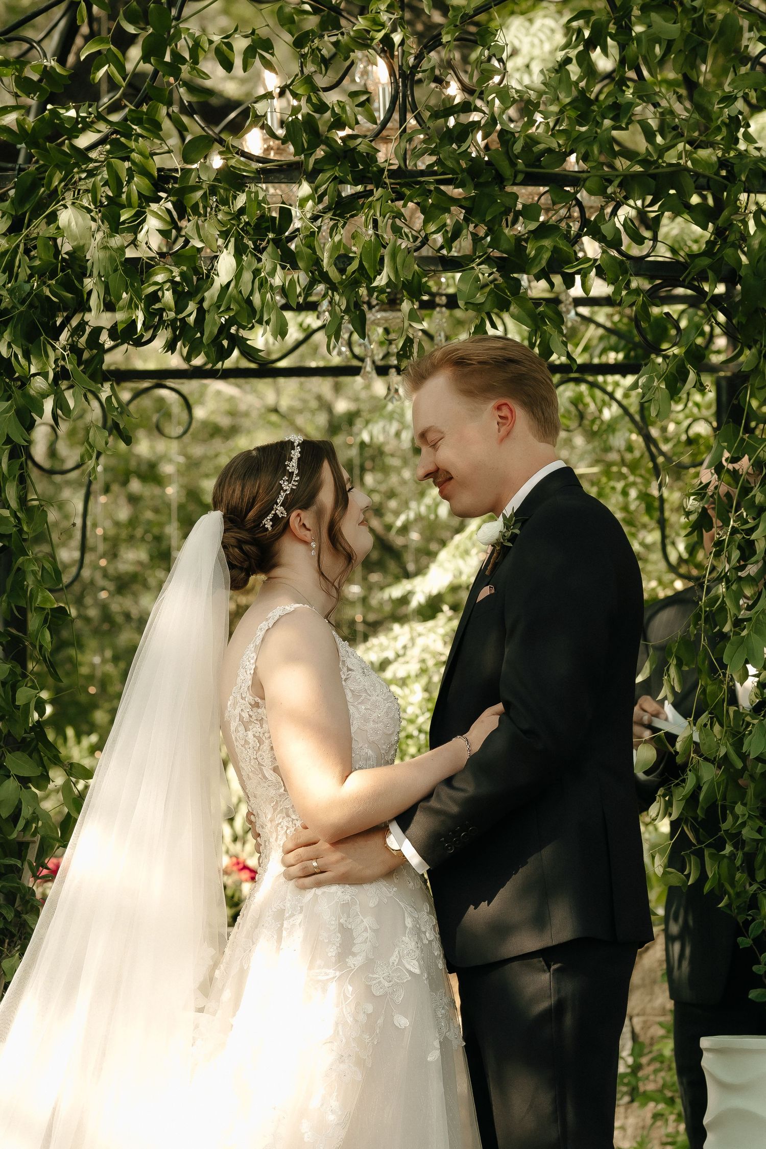 An intimate wedding moment captured beneath a canopy of green leaves during the ceremony.