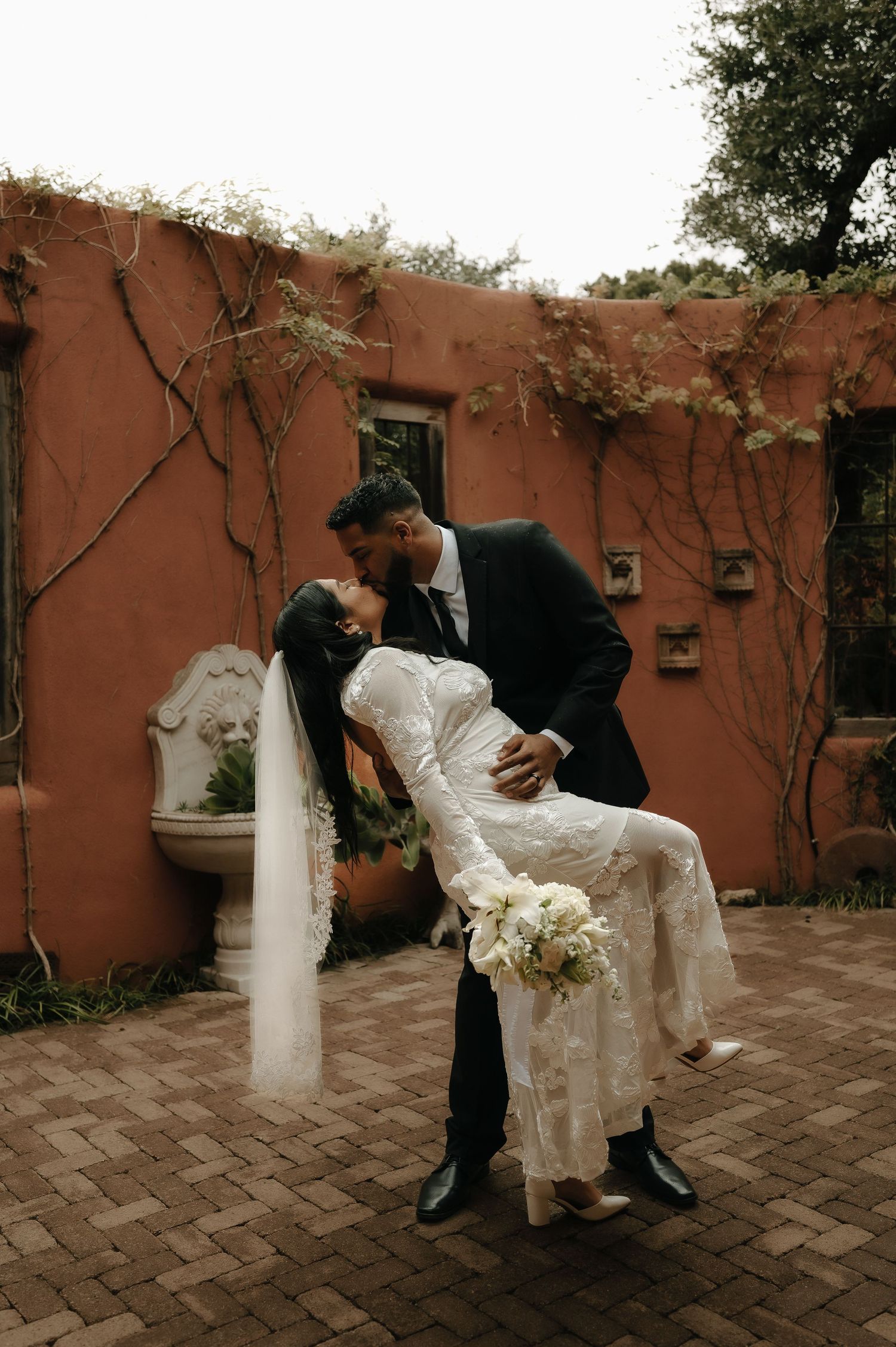 Artistic wedding moment captured against a rustic terracotta wall with herringbone brick pattern.