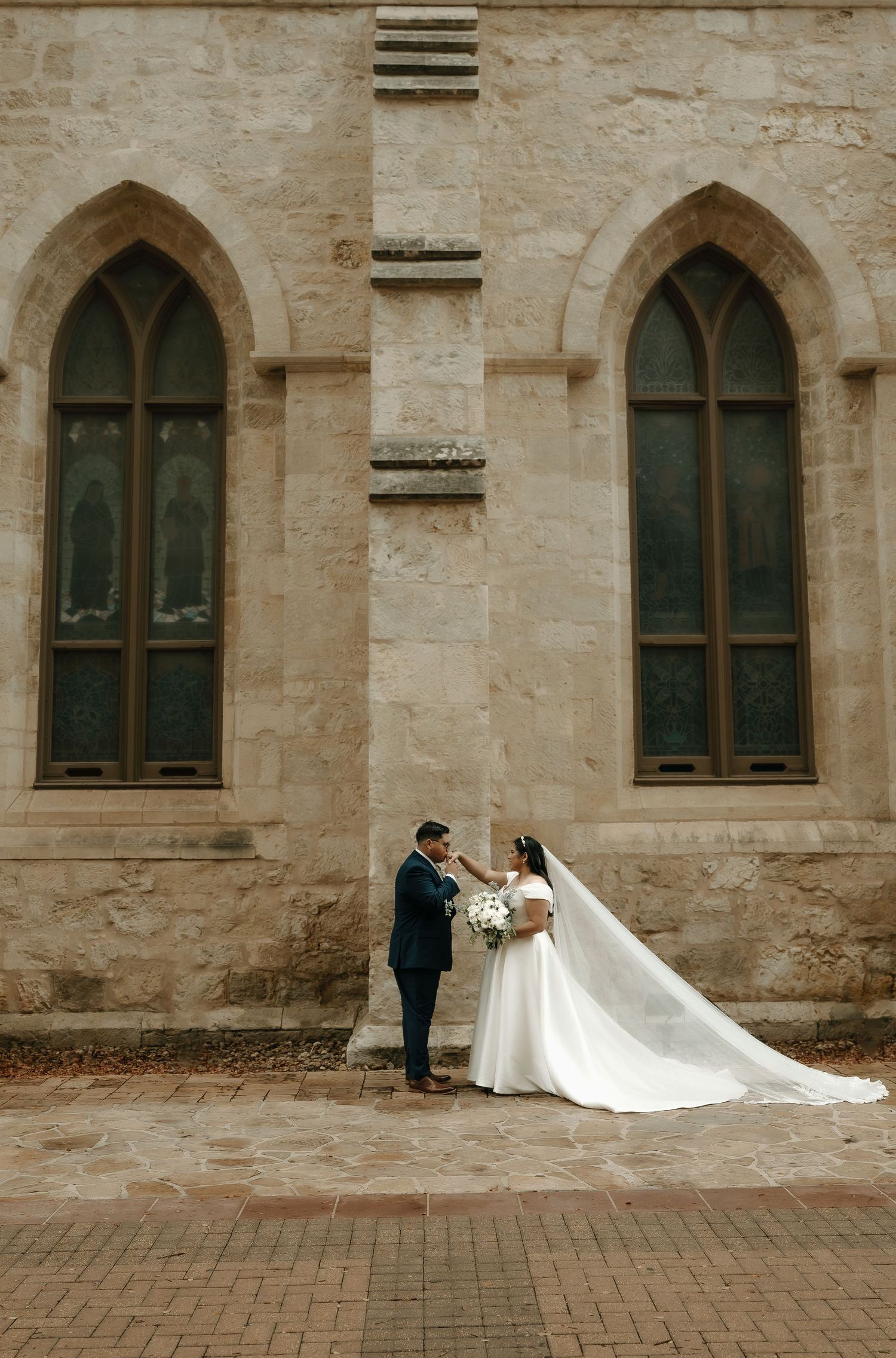 Romantic wedding portrait against historic stone church with Gothic windows.