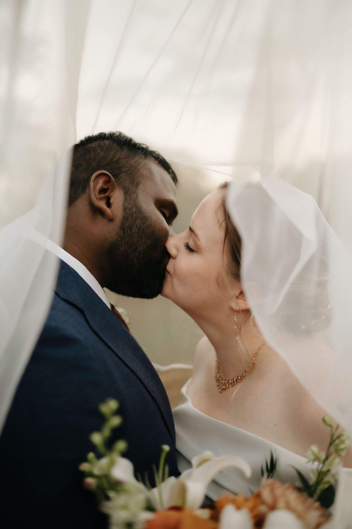 Intimate wedding portrait of couple sharing romantic kiss under bridal veil.