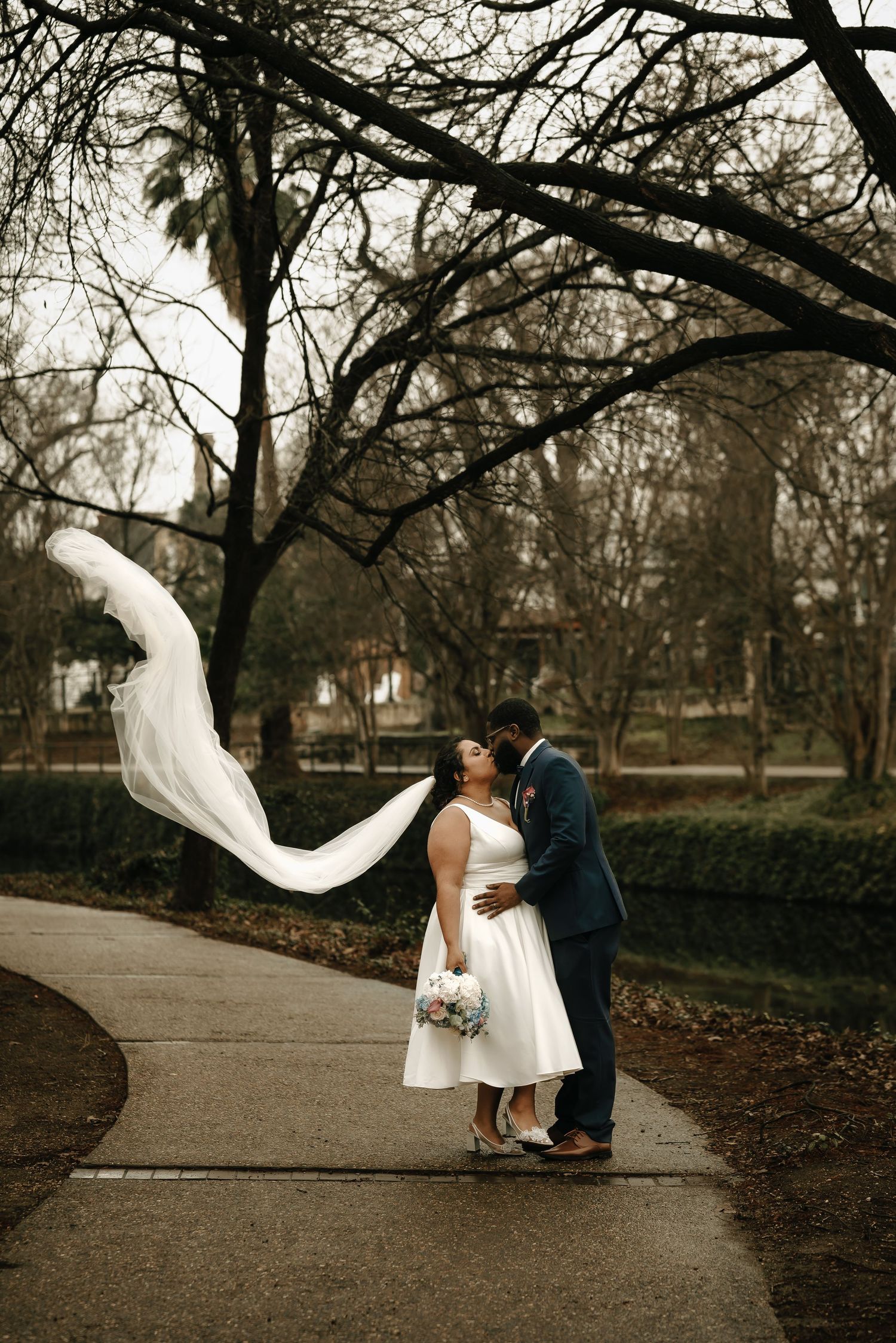 A romantic wedding photo series showing a couple in a park with the bride's veil flowing dramatically in the wind.