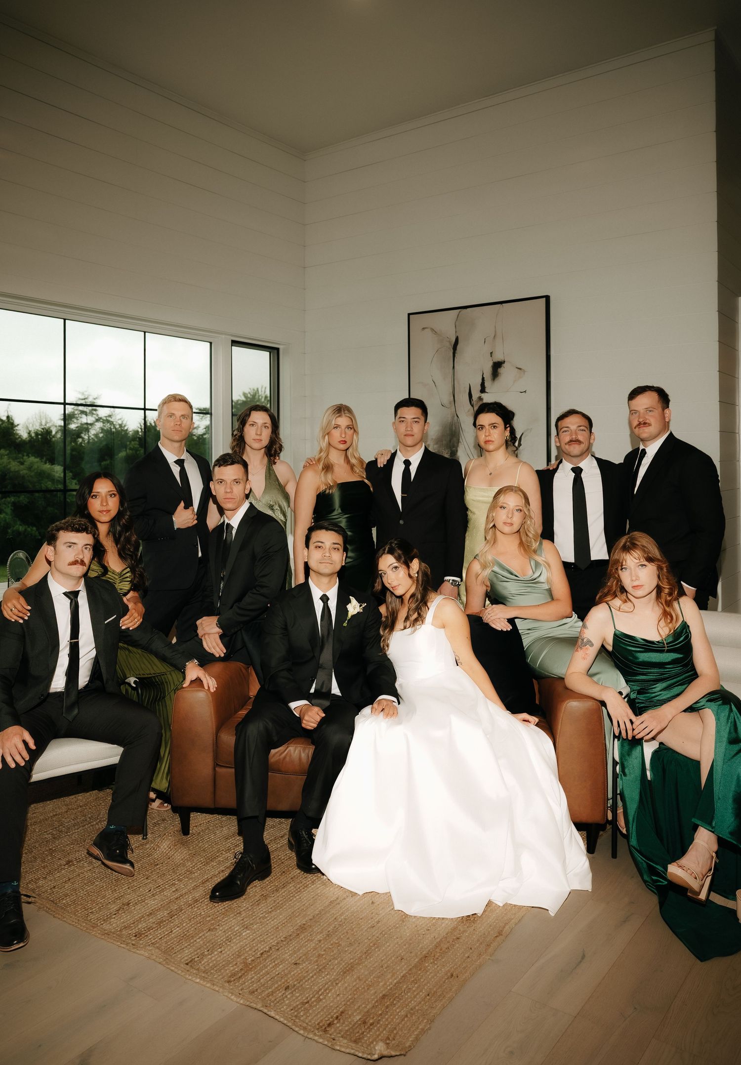 Wedding party group portrait with bride and groom surrounded by guests in black and green formal attire.