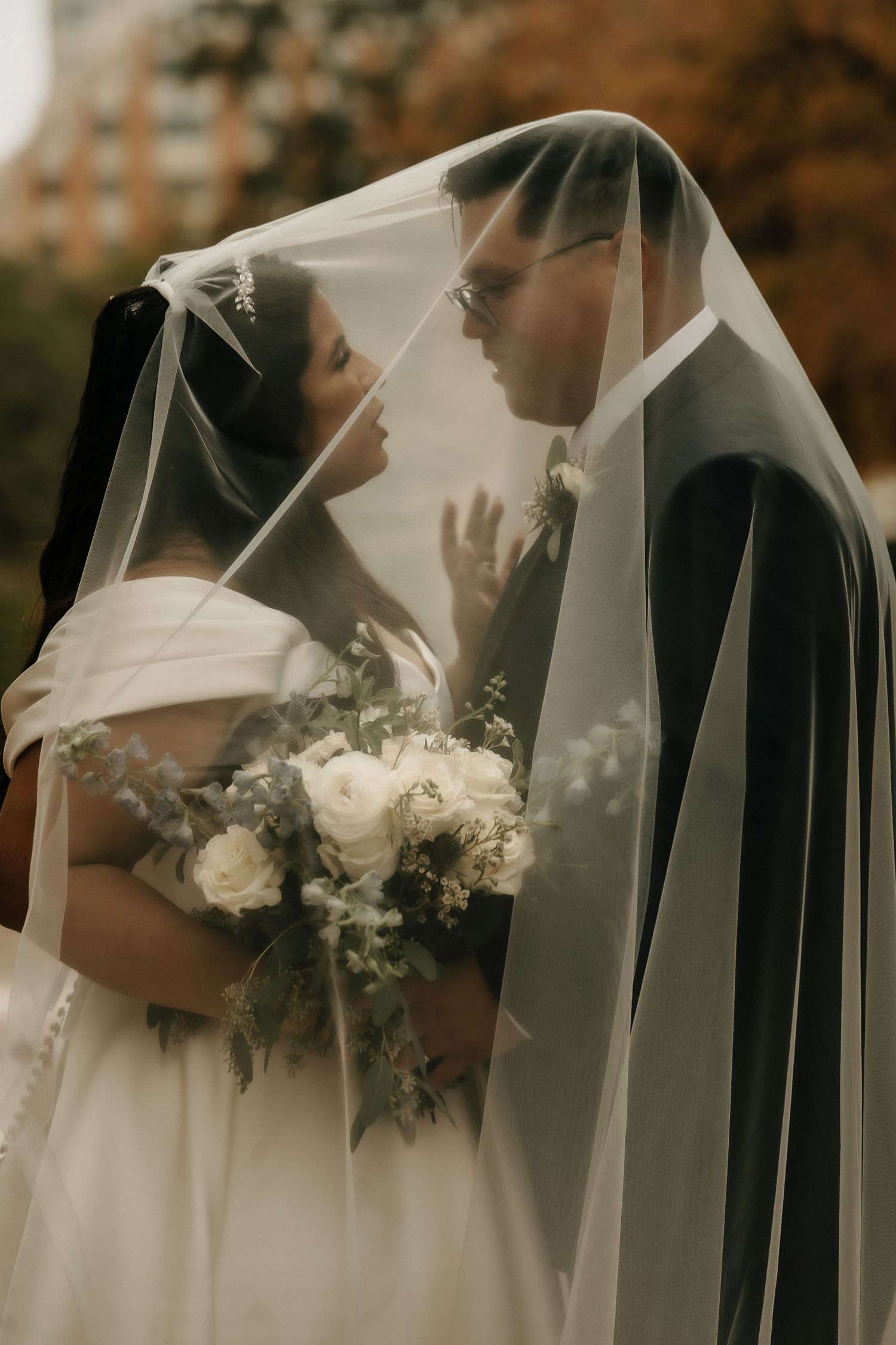 Romantic wedding portrait under a shared veil with white bouquet.