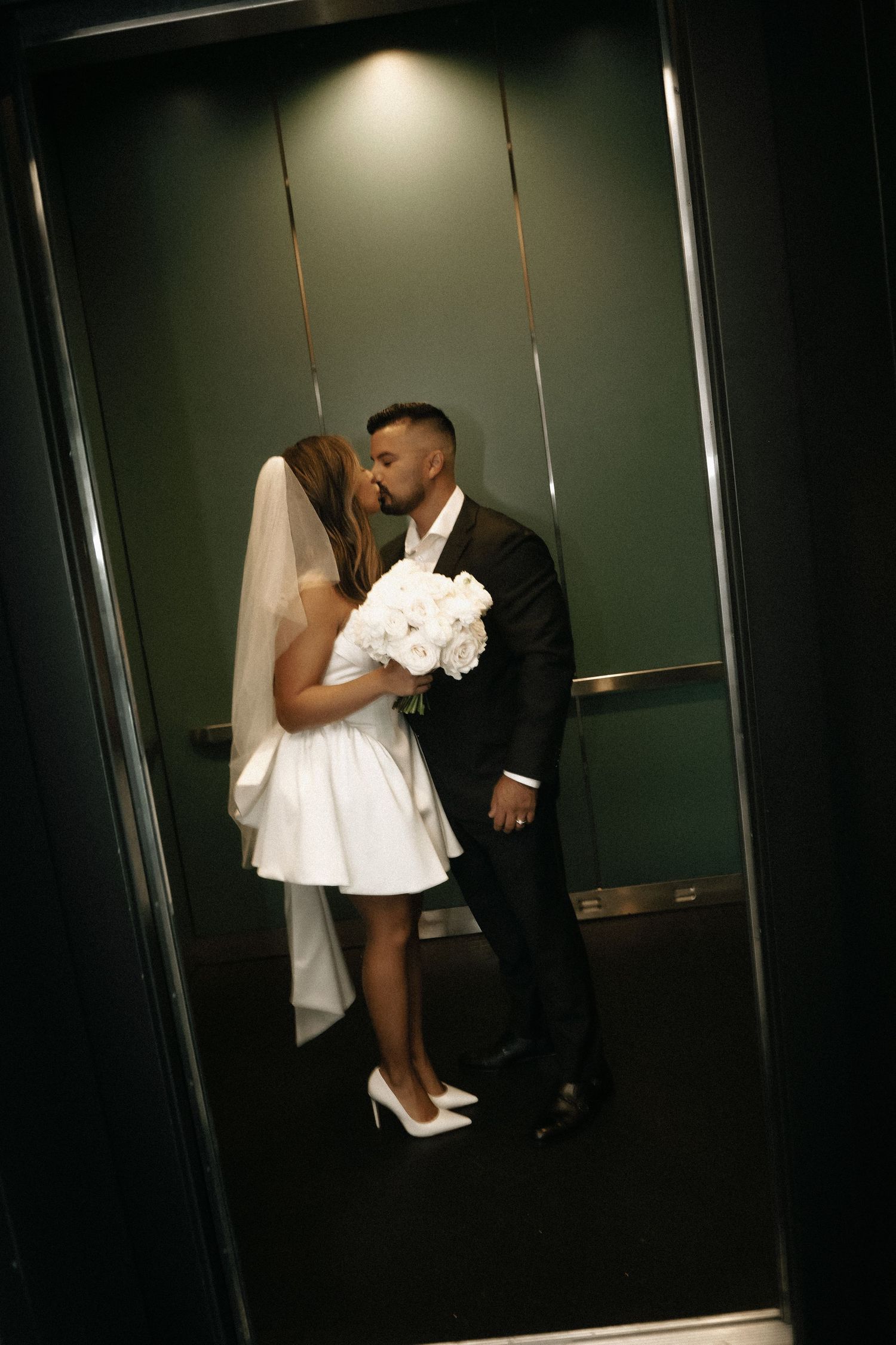 An intimate wedding moment captured in an elevator with a white bouquet.