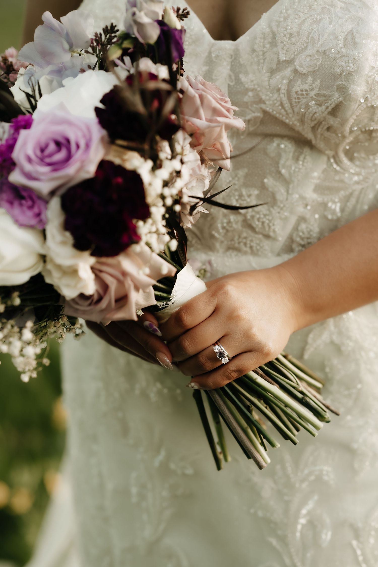 Close-up of bridal bouquet featuring purple roses and mixed flowers with engagement ring detail.
