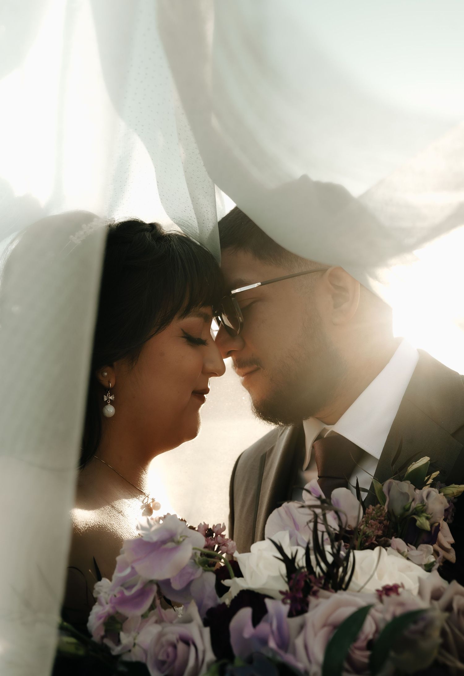 Dreamy wedding portrait through sheer white fabric with purple flowers in foreground.