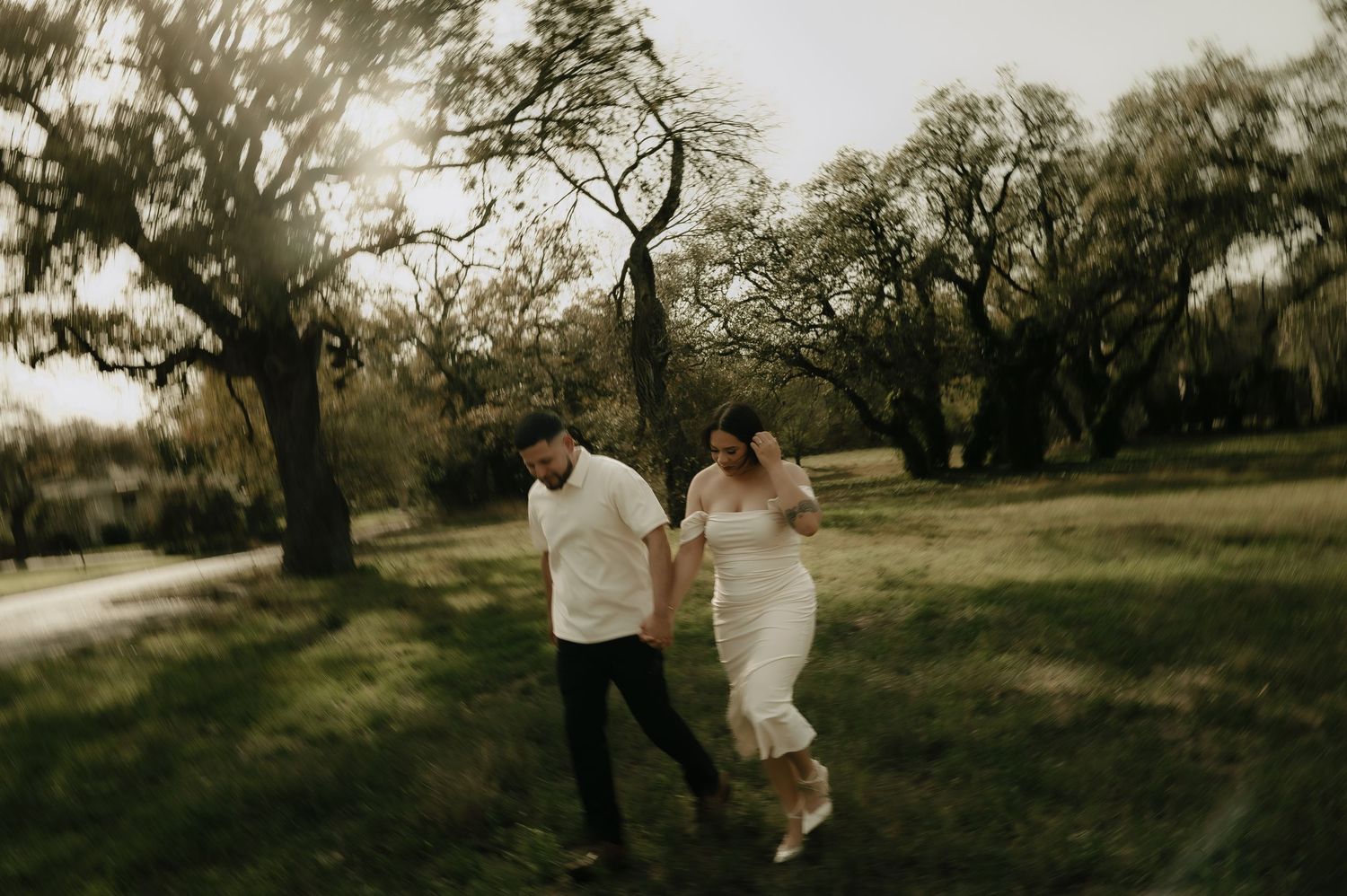Wedding couple dancing and twirling in scenic outdoor field at sunset.