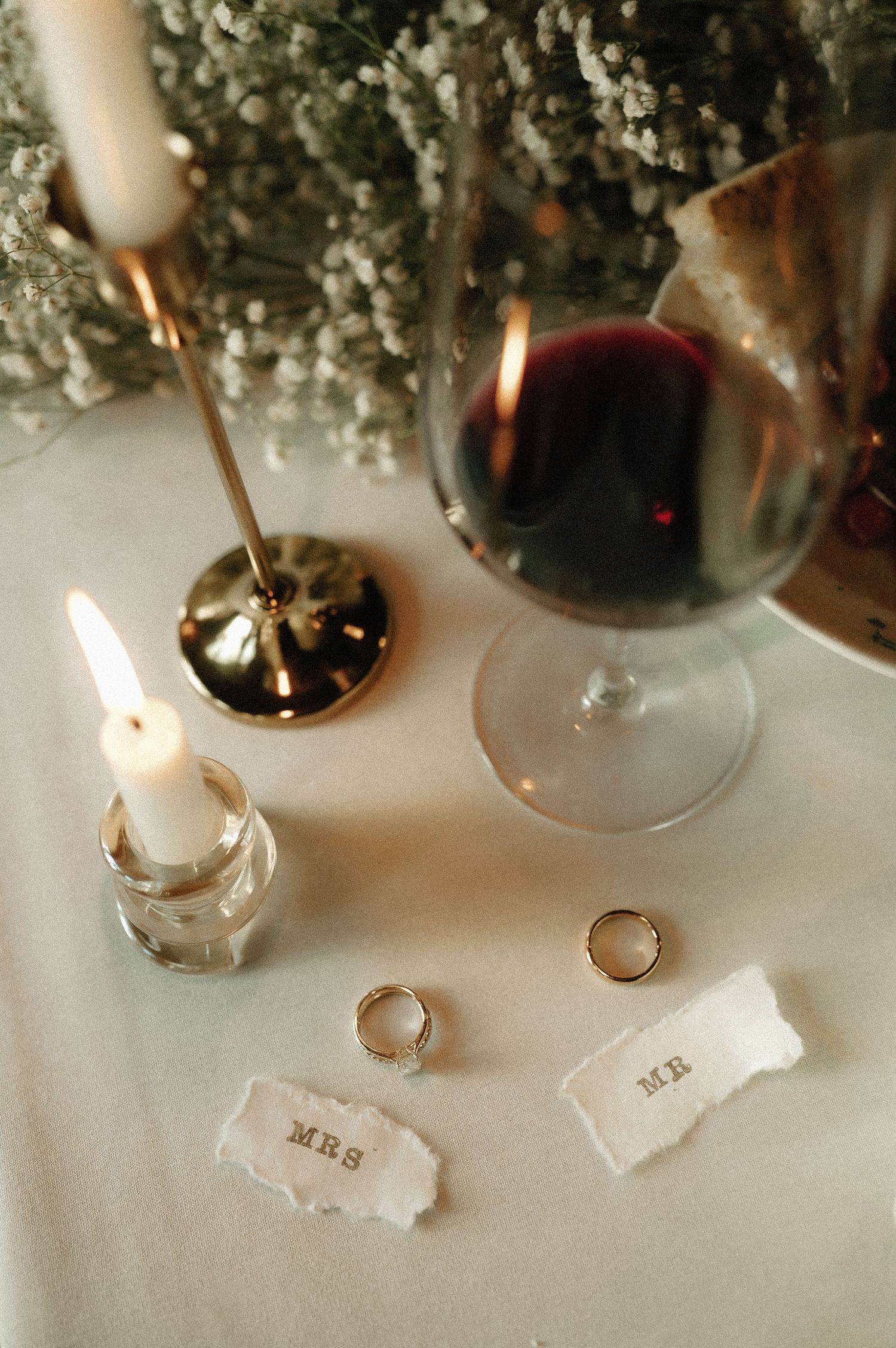 Wedding rings and candles arranged on an elegant white table with floral decorations.