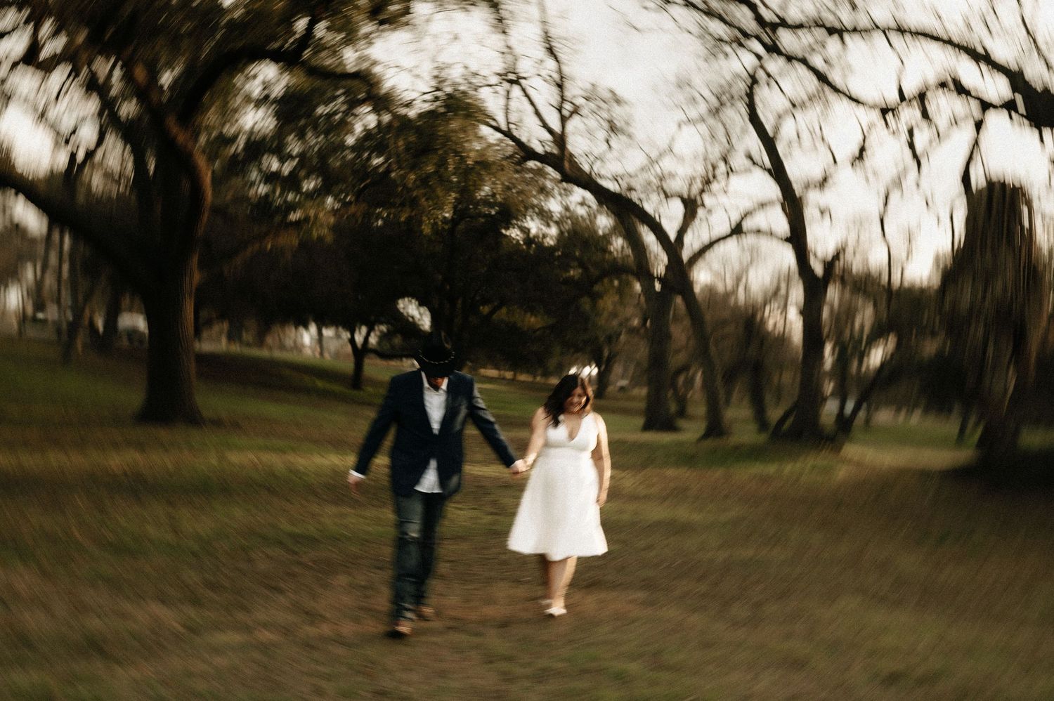A couple in wedding attire walks through a scenic outdoor setting at dusk.