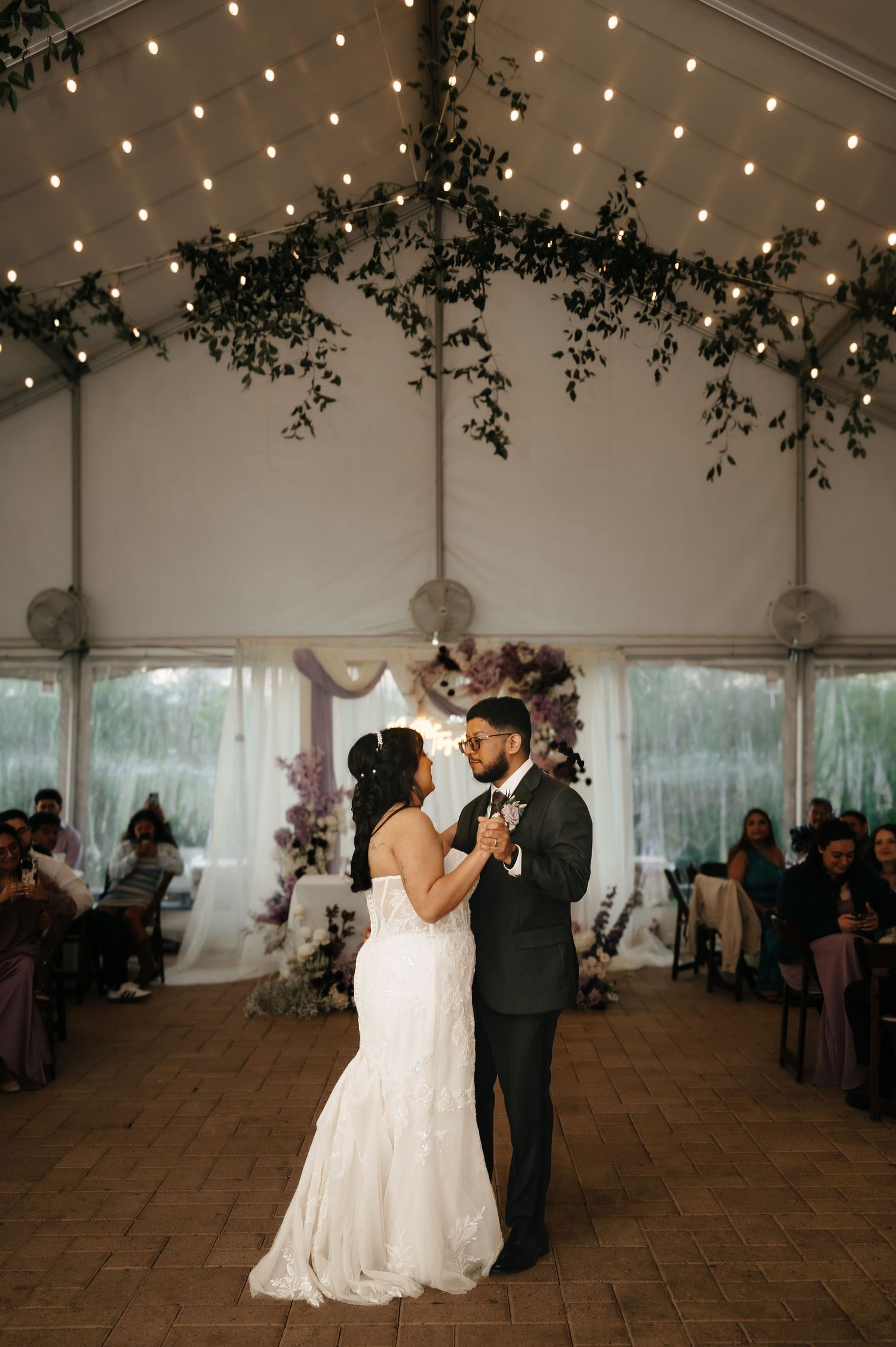 Wedding reception dance in a tent decorated with string lights and greenery.