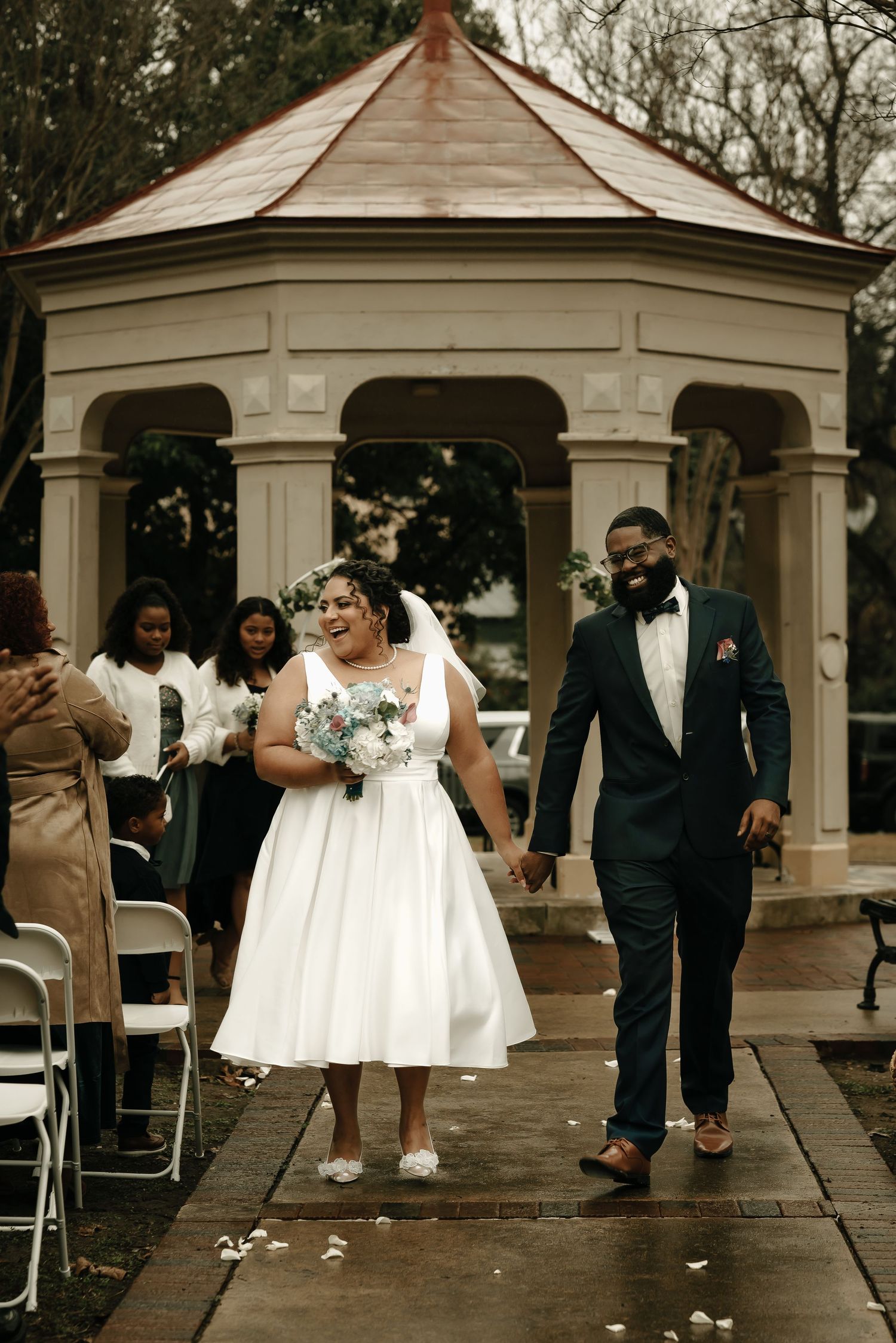 Wedding party celebrates under a white gazebo during an outdoor ceremony.