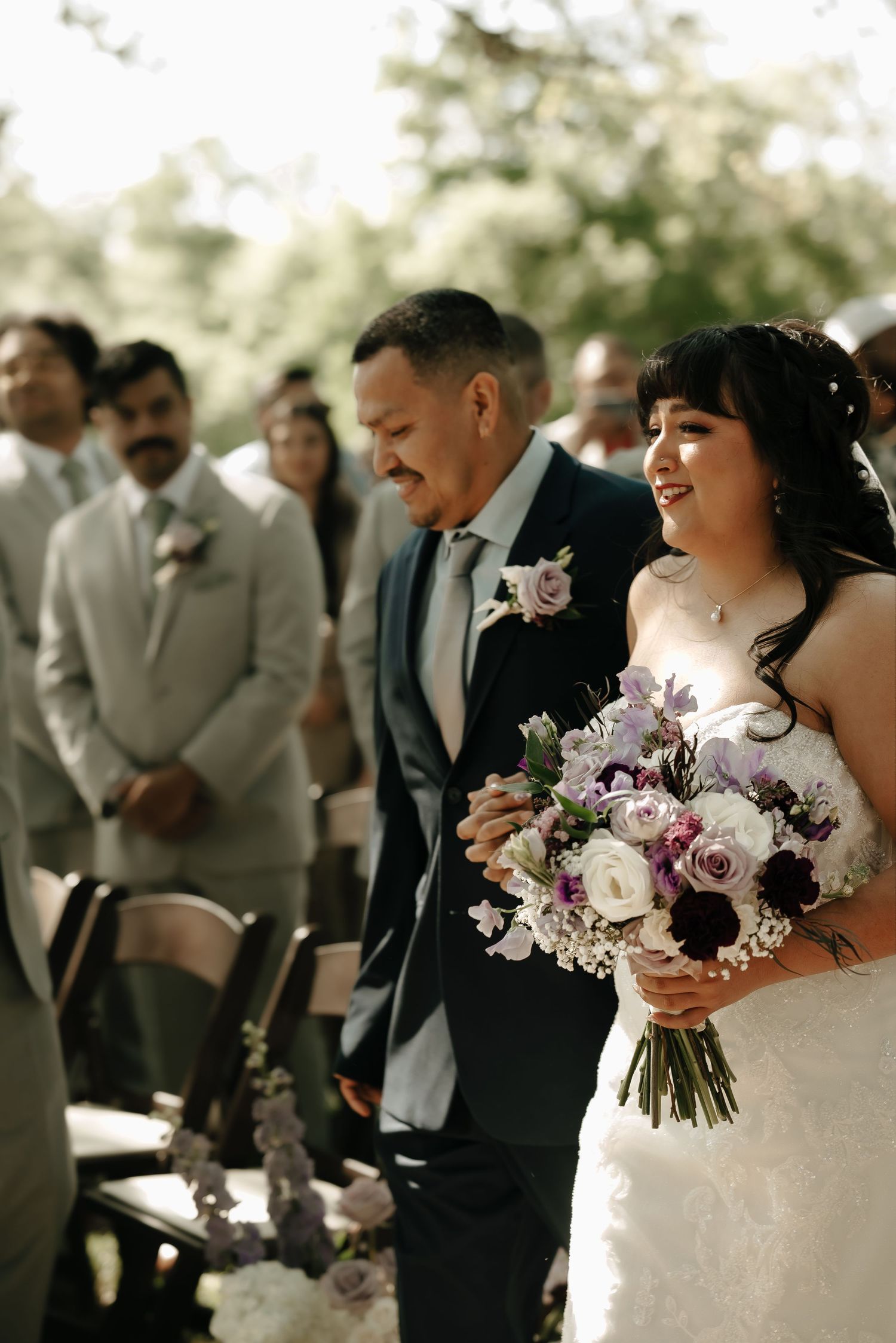 Beautiful wedding bouquet features purple and white flowers against natural backdrop.