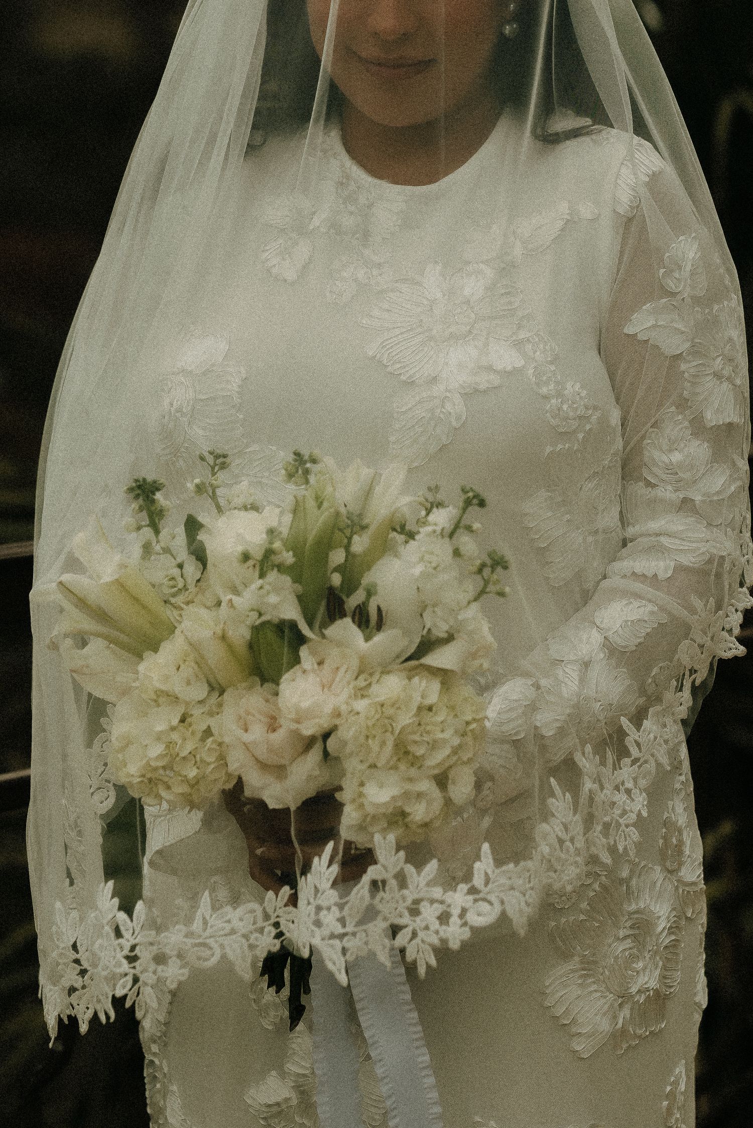 Close-up detail of a delicate white wedding bouquet against lace dress.