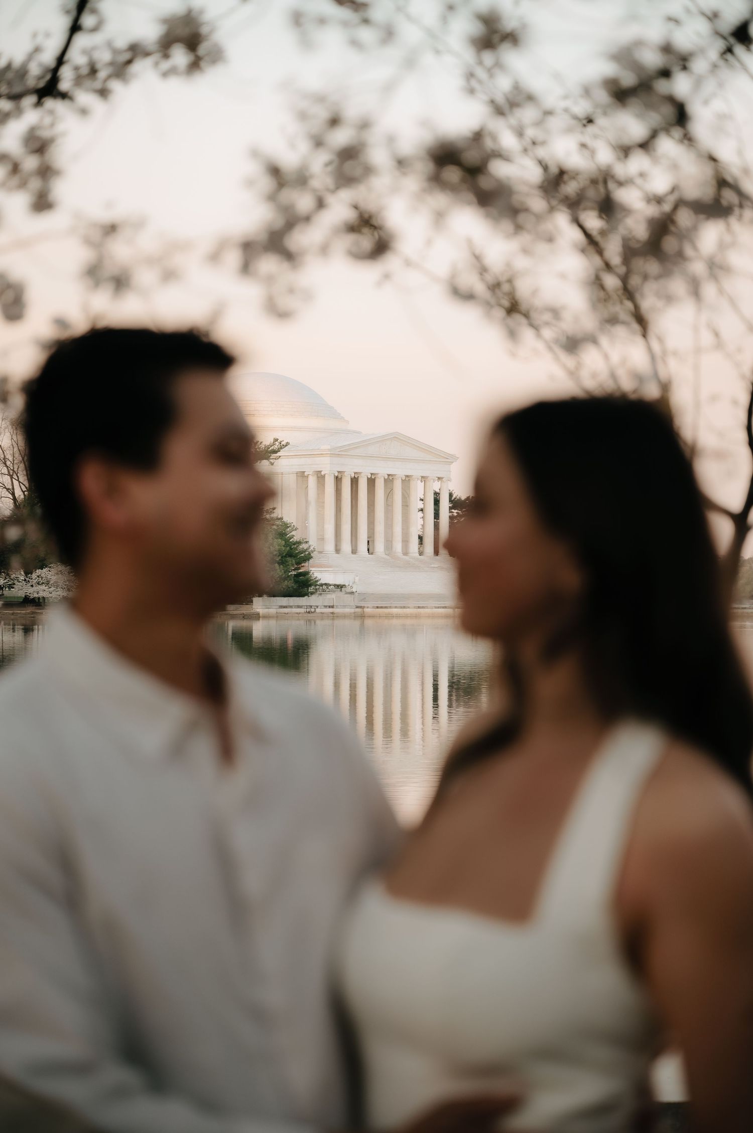 Couple poses in front of the Jefferson Memorial at the Tidal Basin in Washington DC during golden hour.