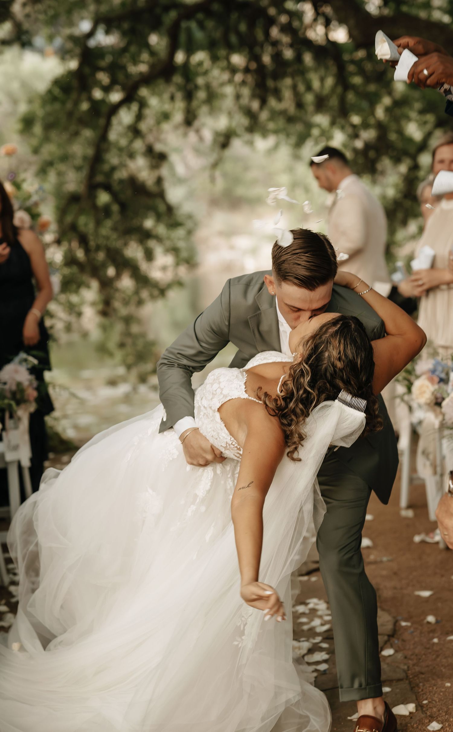 Dramatic dip kiss during wedding ceremony with flower petals scattered on ground.