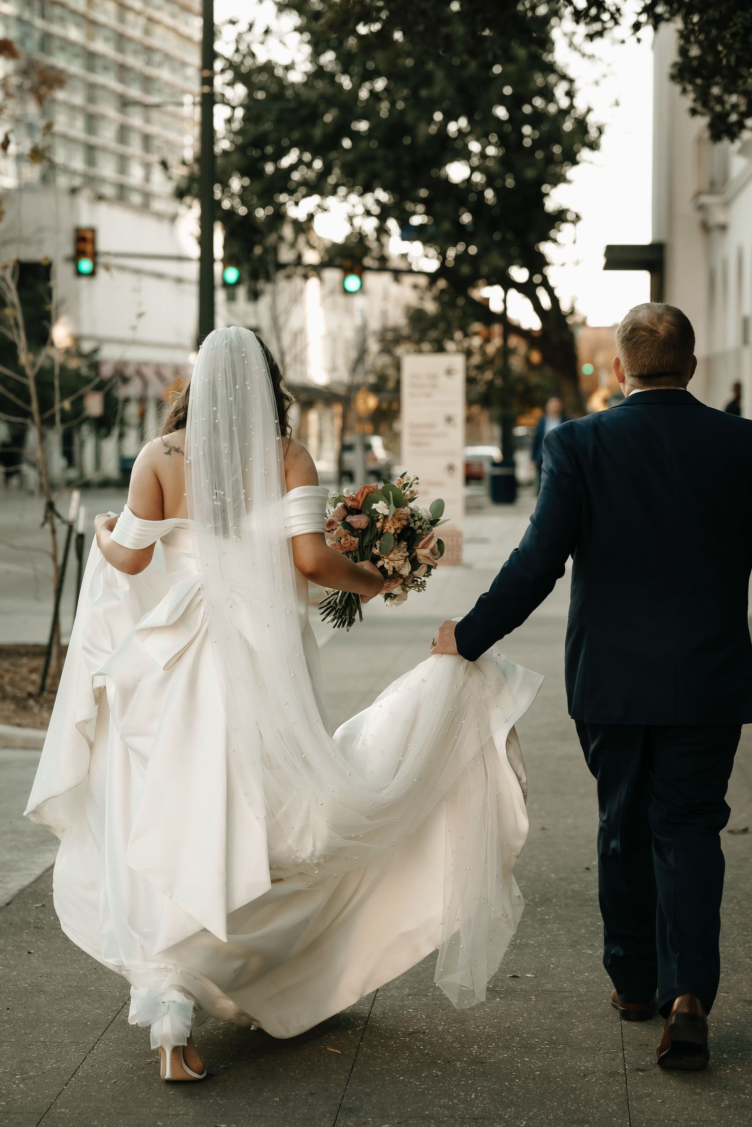 Wedding couple walking down a city street with the bride's dress flowing elegantly behind them.