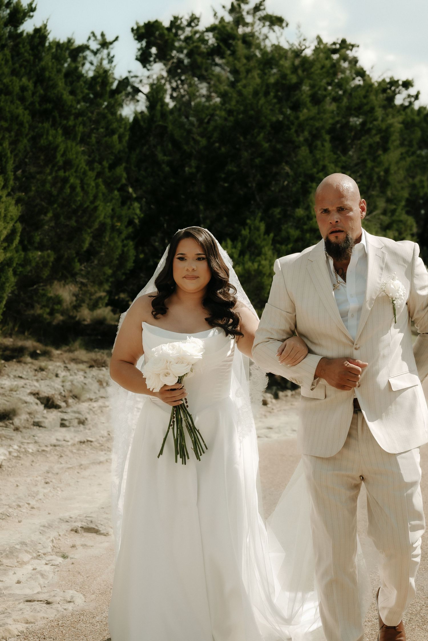 Newlyweds pose for photos on a sunny beach wearing matching white and cream attire.
