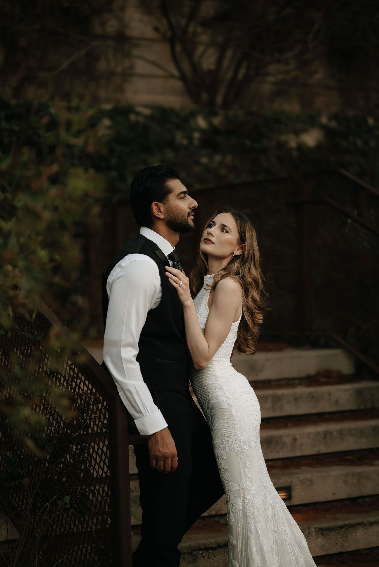 Romantic couple in formal wear embraces on outdoor staircase.