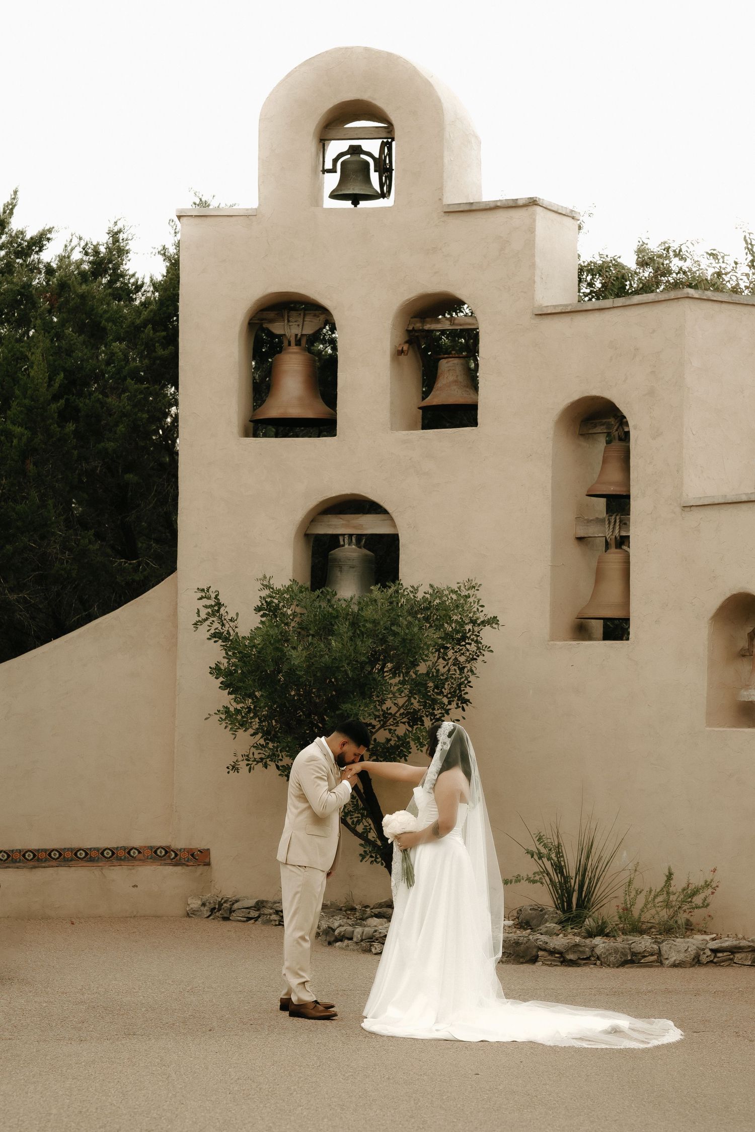 A wedding ceremony in front of a Spanish mission-style bell tower with multiple arched openings.