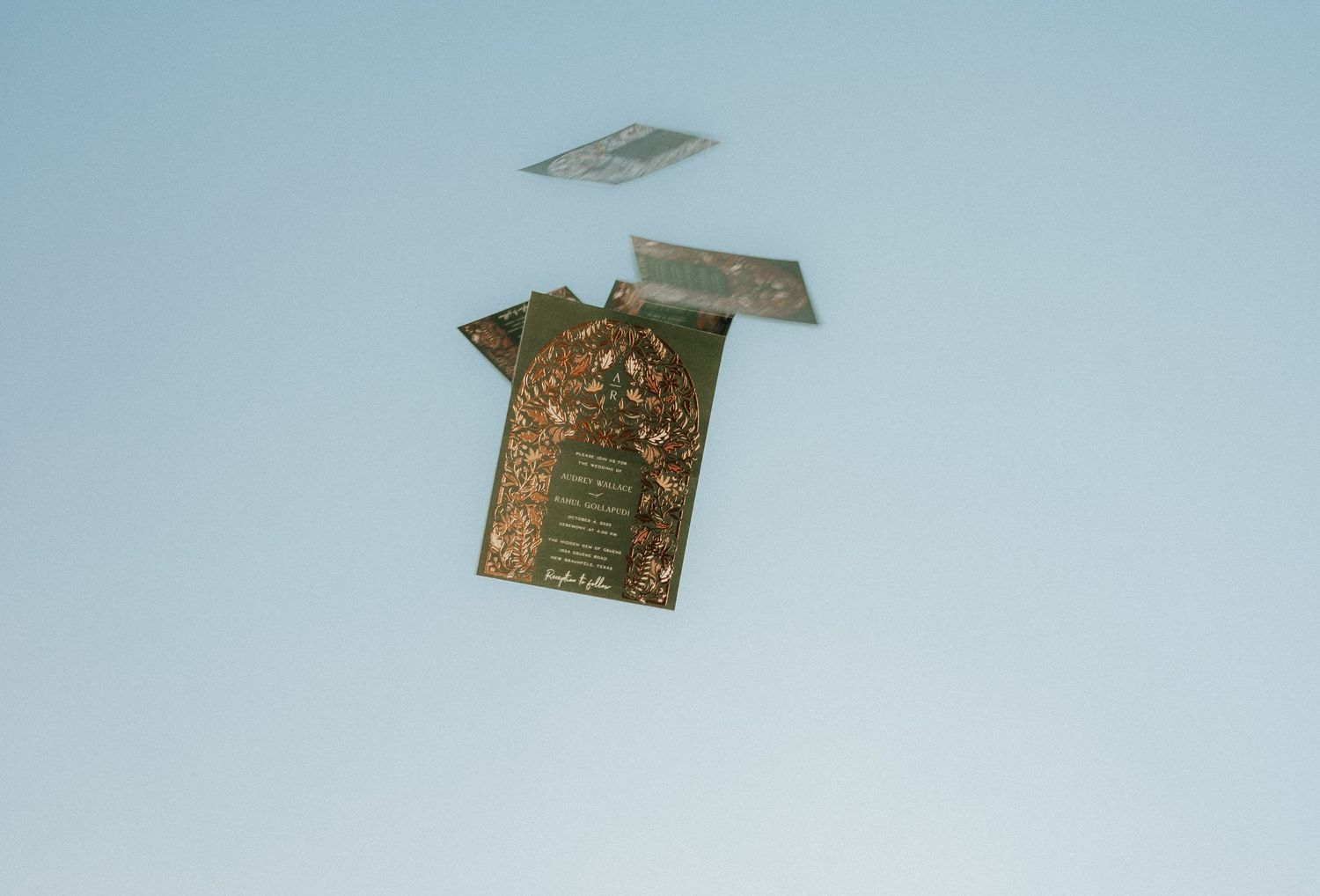 Gold wedding invitations floating against light blue background.