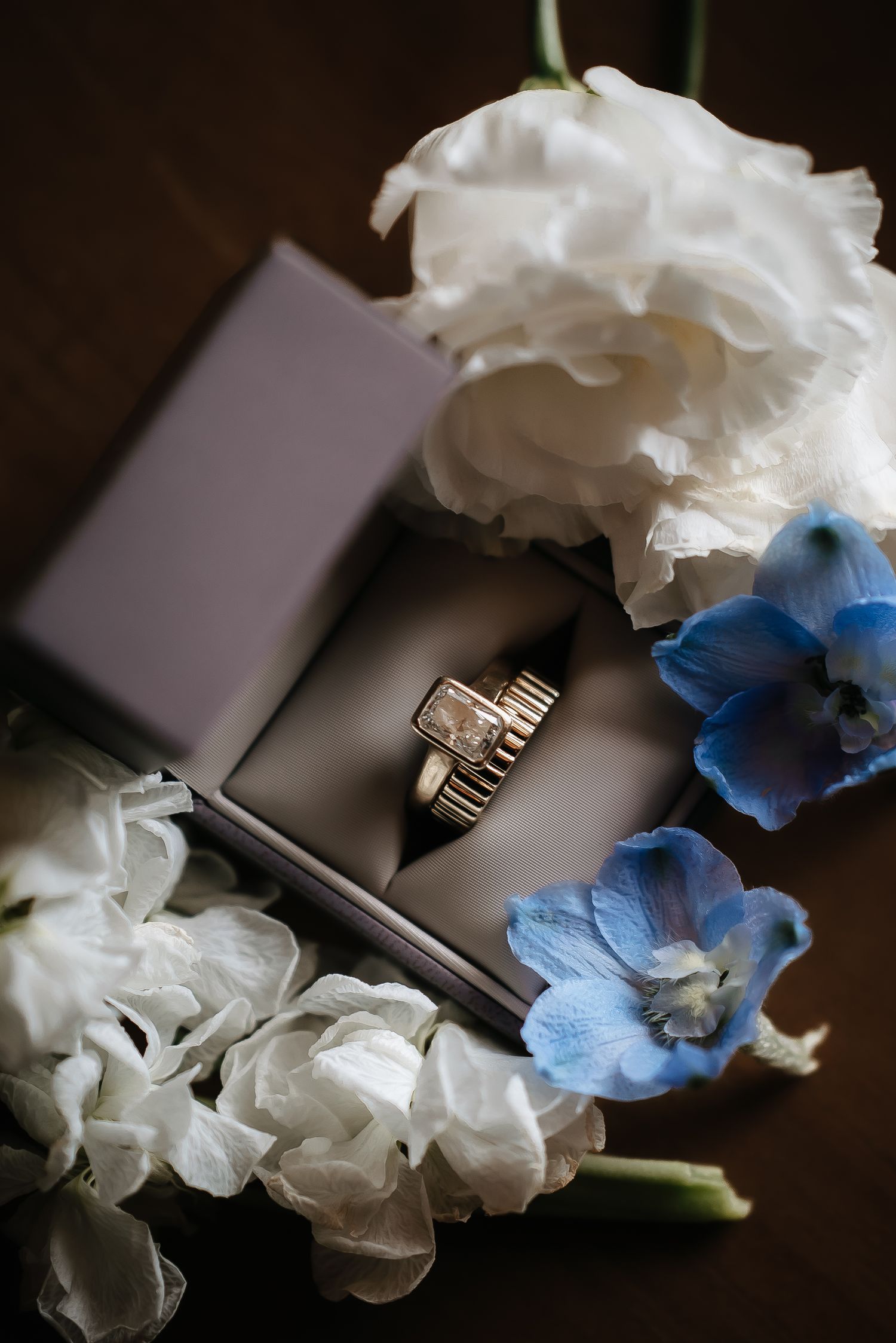 Wedding rings displayed with white and blue flowers in elegant composition.