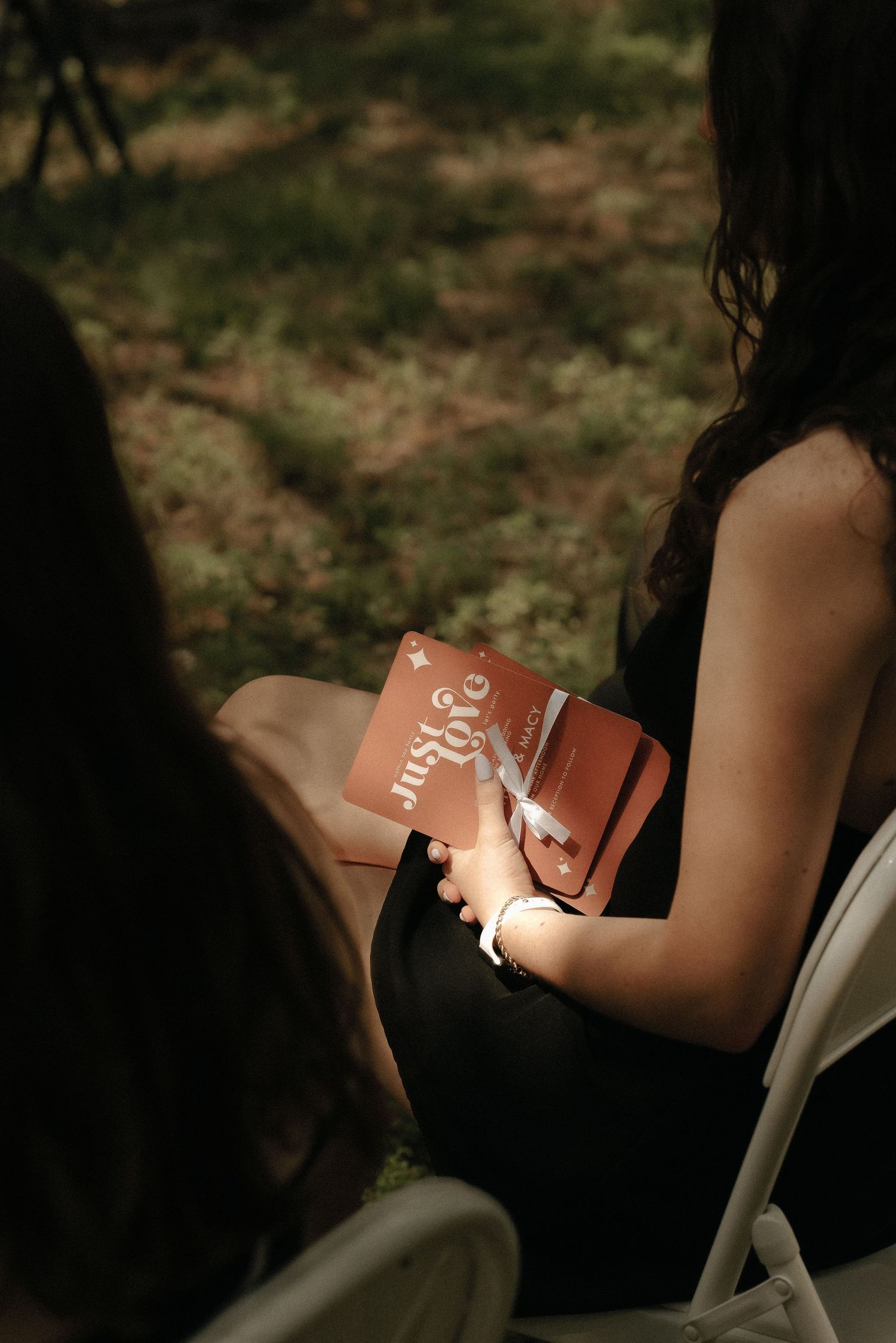Guests hold small pink books during an outdoor wedding ceremony.