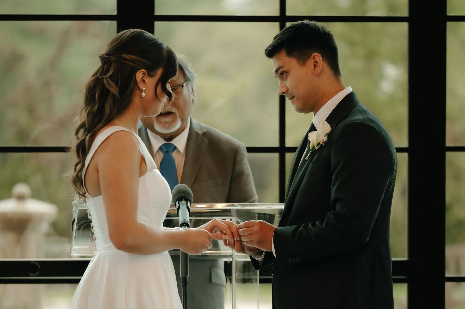 Groom places wedding ring on bride's finger at altar with officiant during elegant indoor ceremony.
