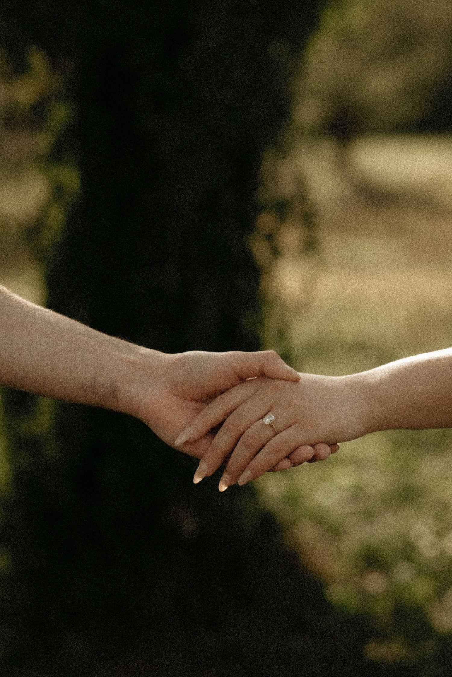 Close-up of hands with wedding ring holding each other against a blurred natural background.