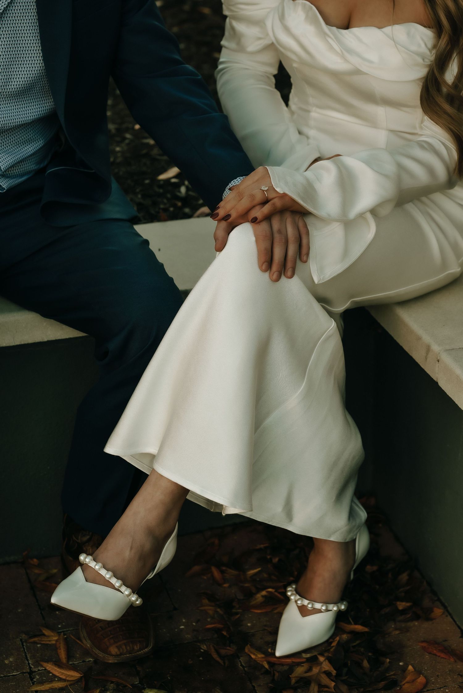 Close-up of white wedding dress and formal shoes on autumn leaves.