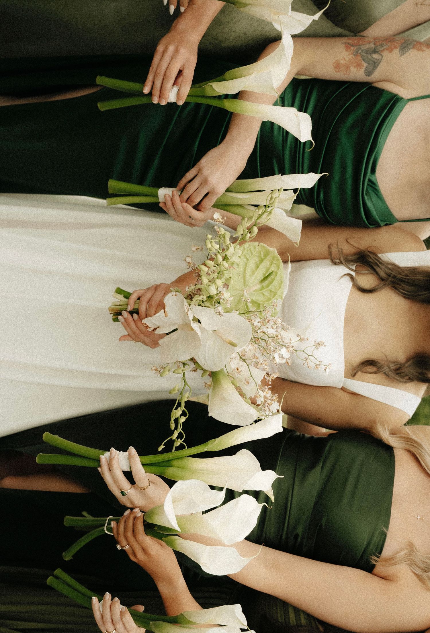 Bride and bridesmaids in emerald green dresses holding white calla lily bouquets, aerial view wedding party photo.