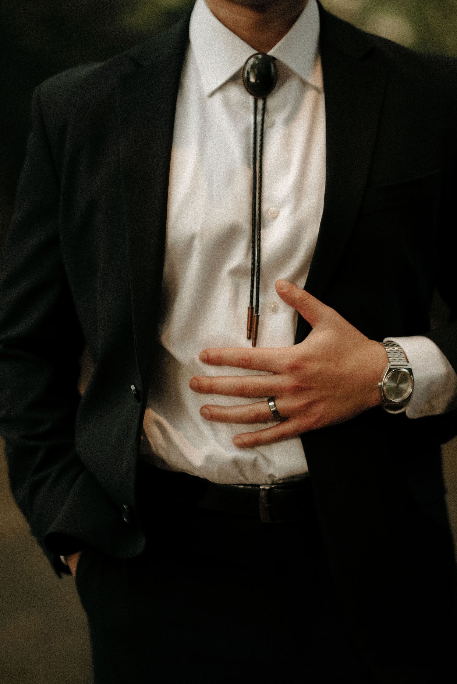 Groom adjusts bolo tie on white shirt with black suit jacket.