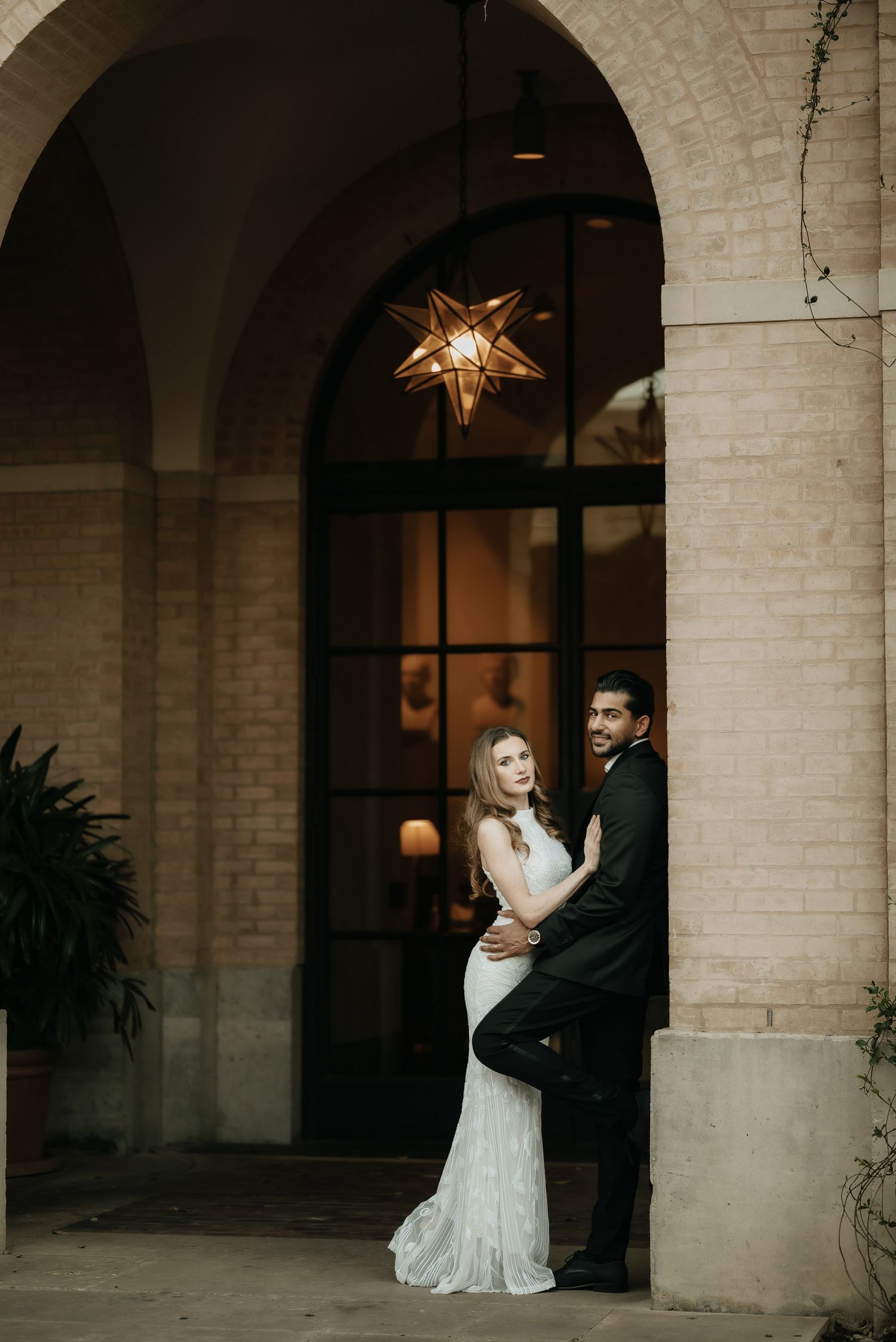 Elegant couple poses under illuminated star light in arched brick doorway.