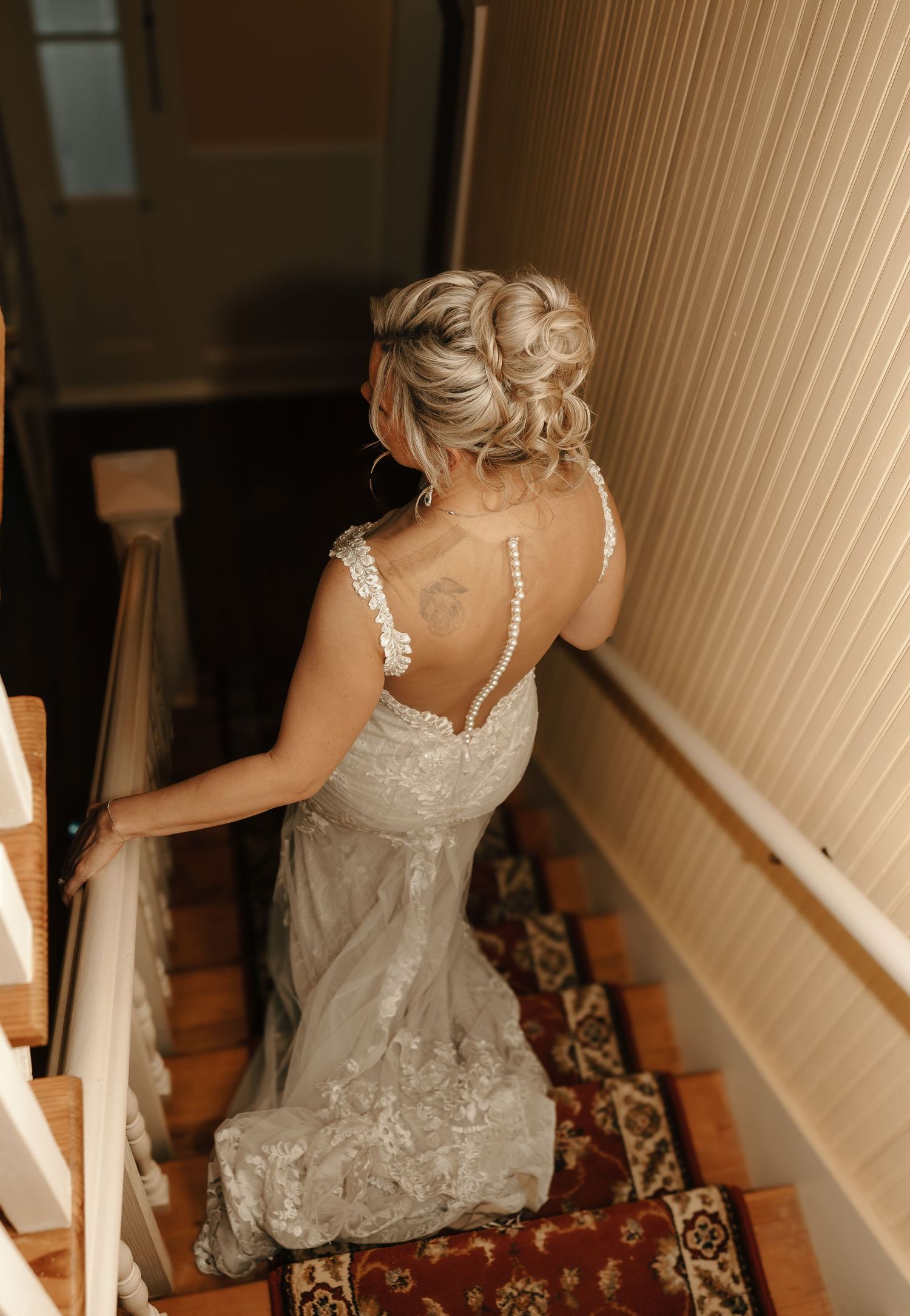 Bride in lace wedding gown descending staircase with ornate carpet runner.