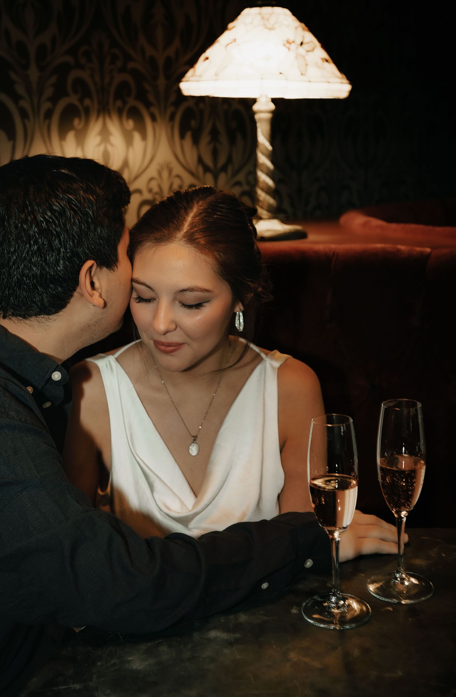 A romantic couple shares an intimate moment at a candlelit table with champagne glasses.